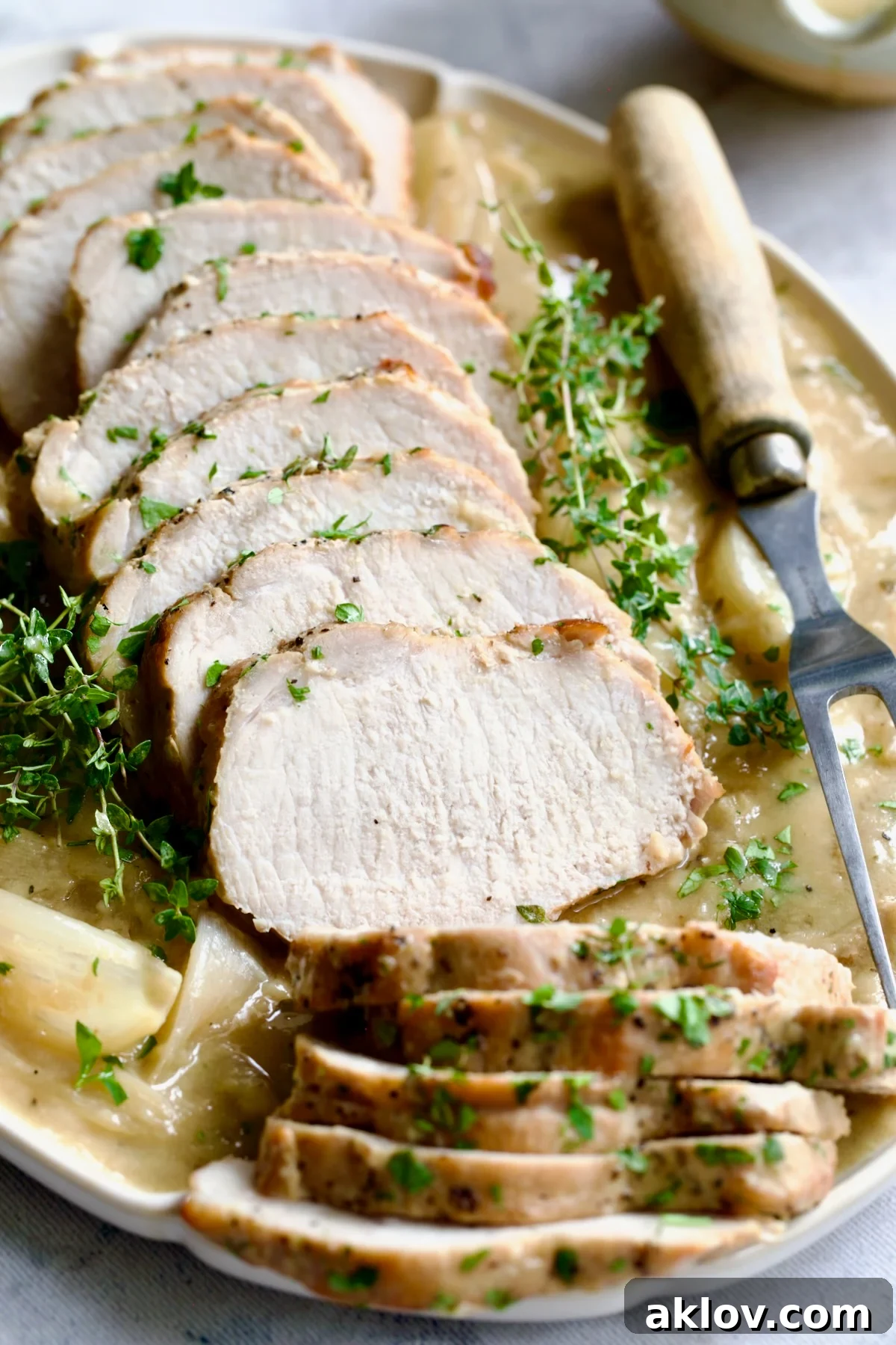 Perfectly sliced Braised Pork Loin in Dijon Mustard Sauce on an elegant scalloped oval platter, ready to be served with a meat fork and fresh thyme sprigs.