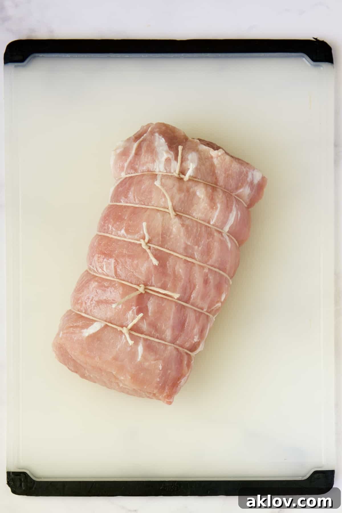 Pork loin roast on white plastic cutting board.