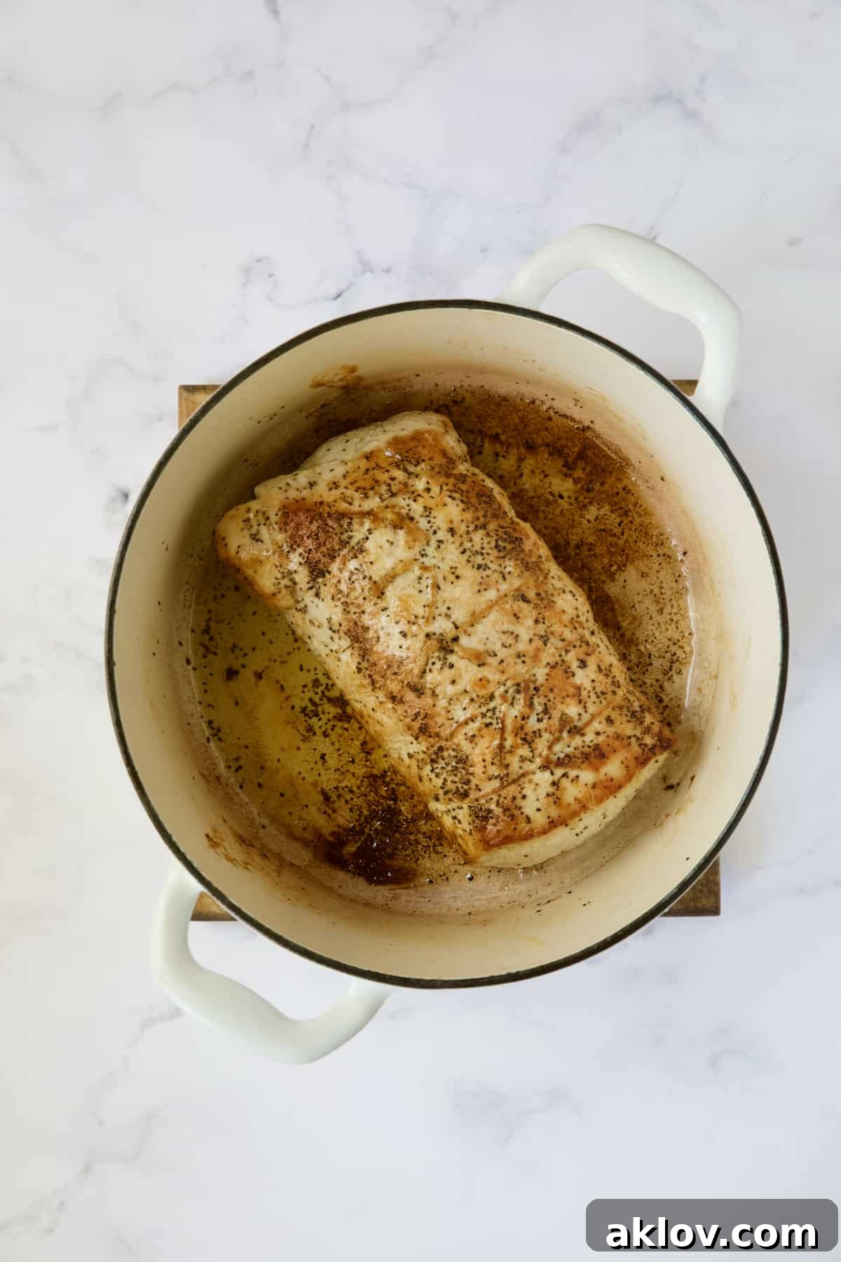 A beautifully browned pork loin searing in a white Dutch oven, creating a rich crust before braising.