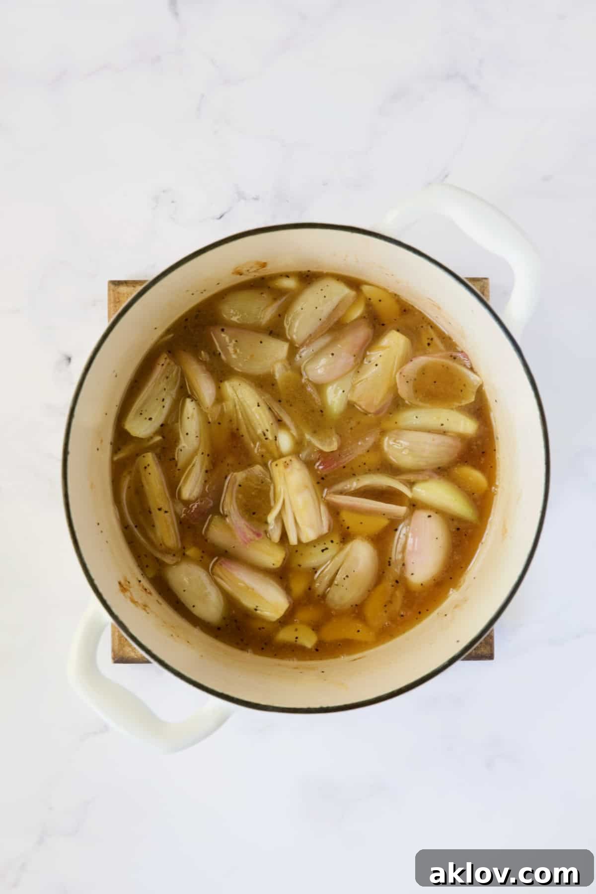 Shallots and garlic simmering with braising liquid in a white Dutch oven, releasing their savory aromas.