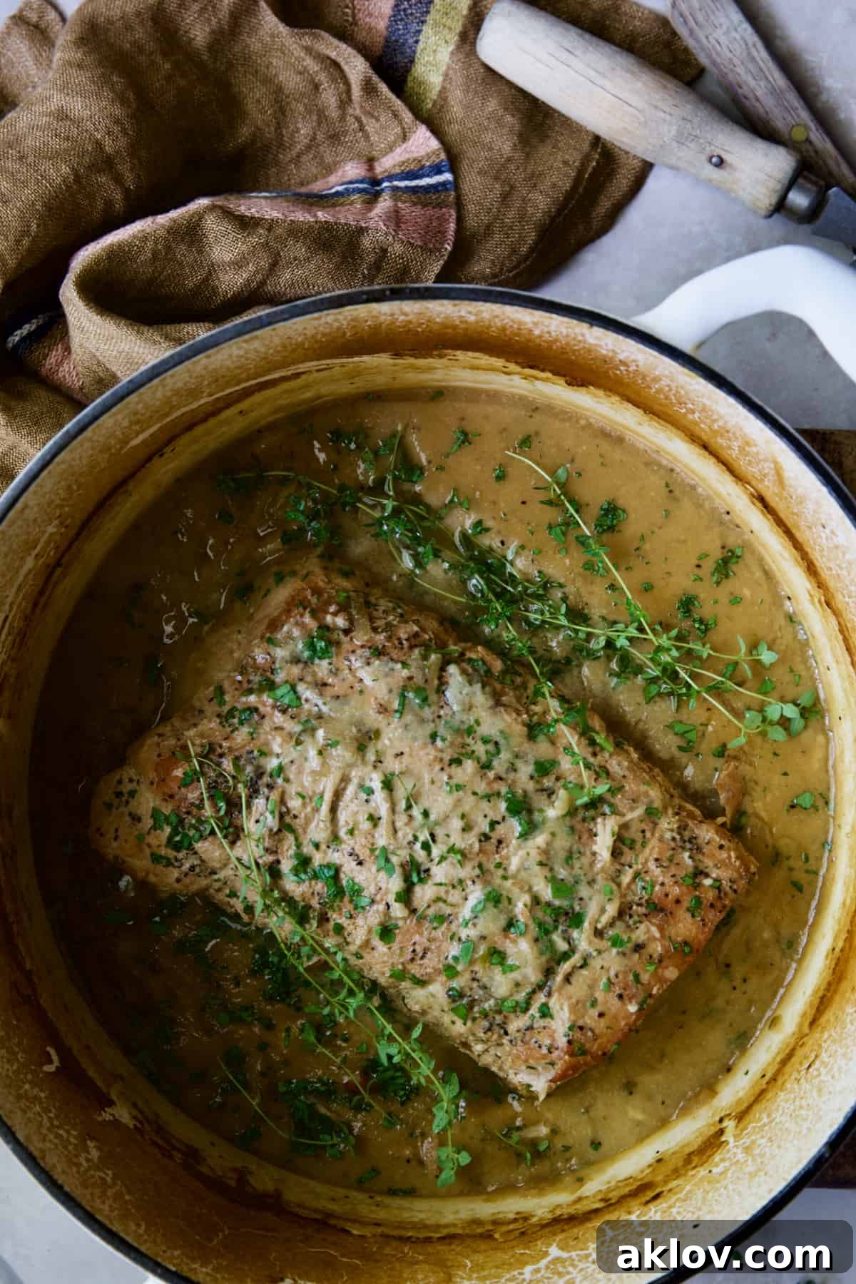 The braised pork loin roast simmering in its rich Dijon mustard sauce inside a white Dutch oven, nearing completion.