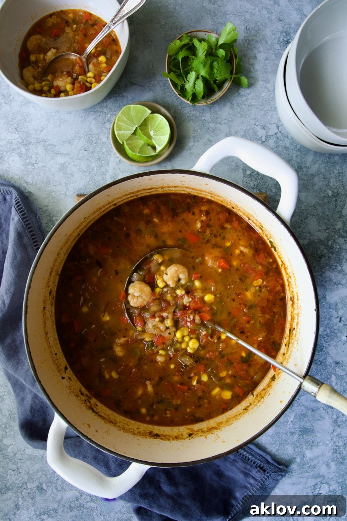 A ladle serving a generous portion of freshly cooked Shrimp and Corn Soup from a white Dutch oven into a bowl, steaming and ready.