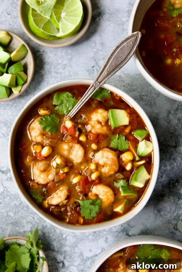 Shrimp and Corn Soup in white bowl with soup spoon garnished with cilantro and lime wedge.