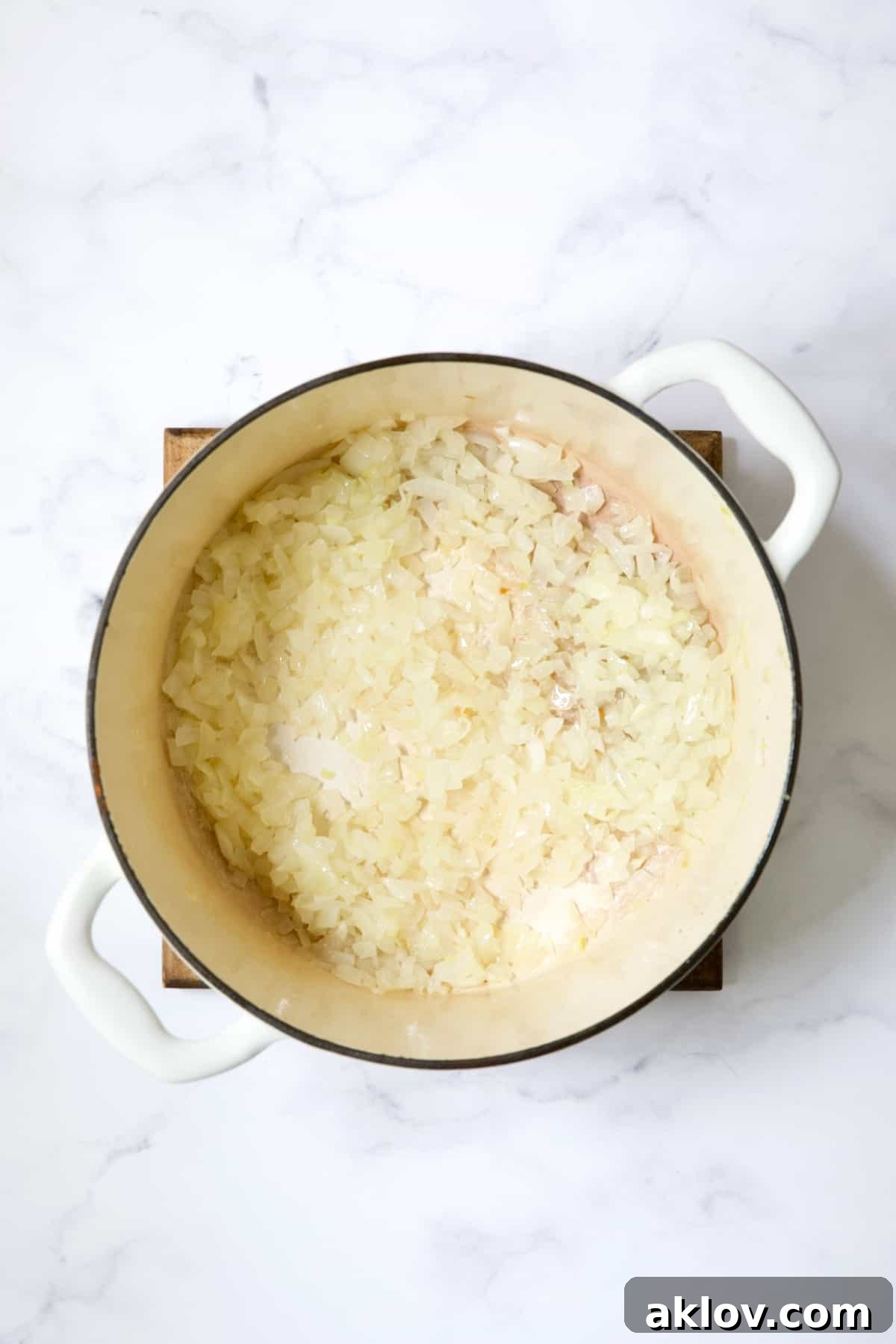 Sautéed onions softening in a white Dutch oven, forming the base of the soup.