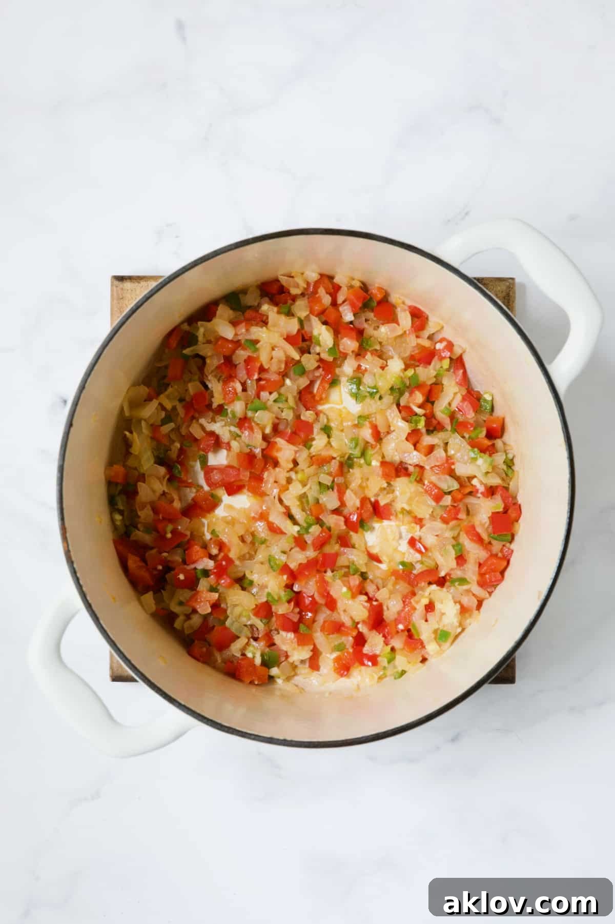 Onions, red bell pepper, and jalapeño sautéing together in a white Dutch oven, developing their flavors.