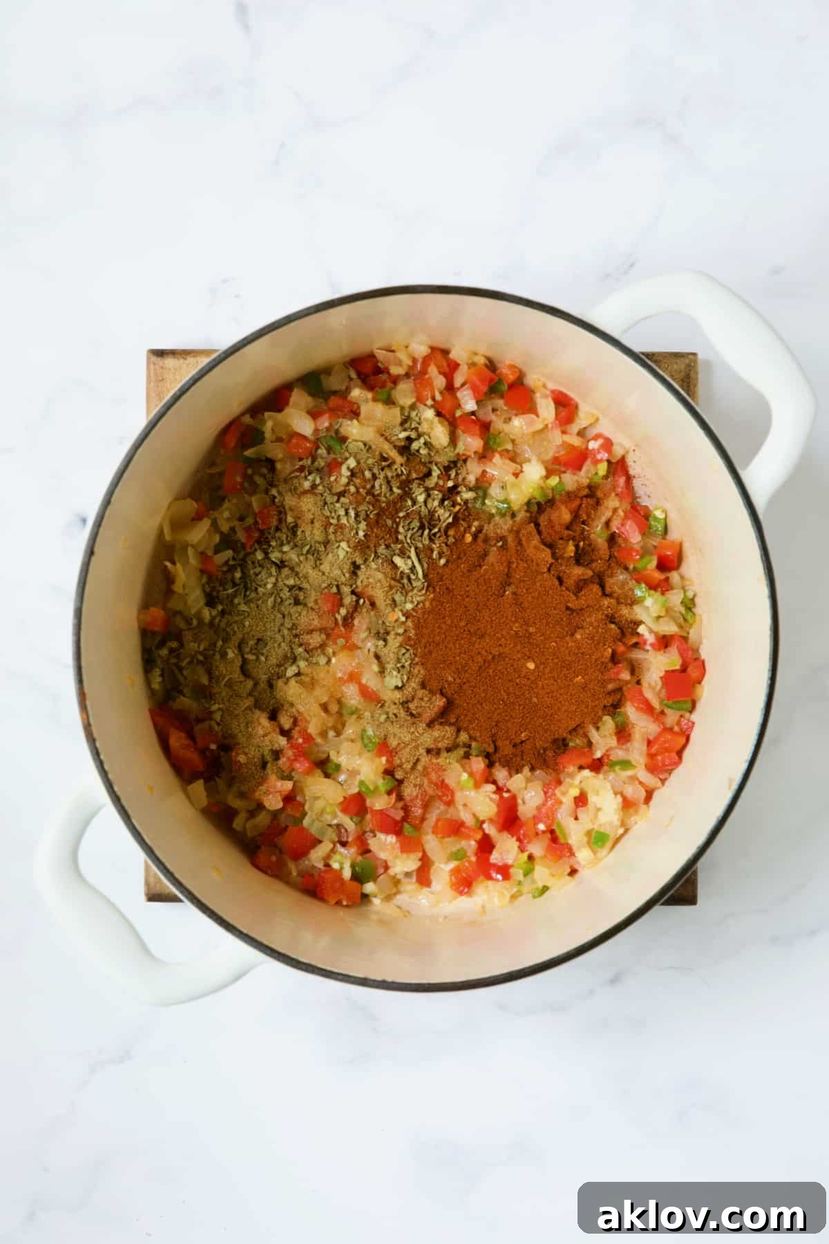 Garlic and a blend of vibrant spices added to the sautéed vegetables in a white Dutch oven, ready to be fragrant.