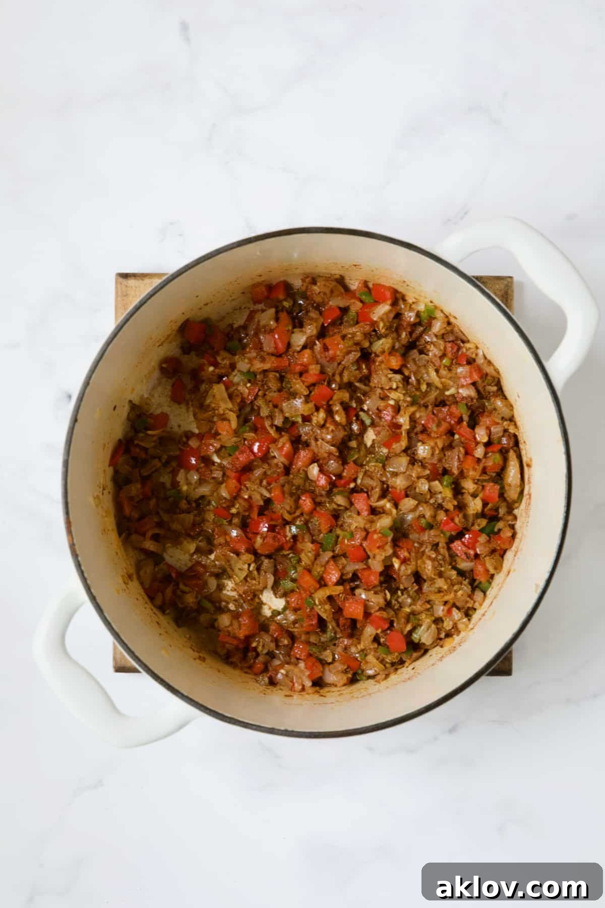 Sautéed vegetables thoroughly coated with a flavorful spice blend in a white Dutch oven, creating a rich base for the soup.