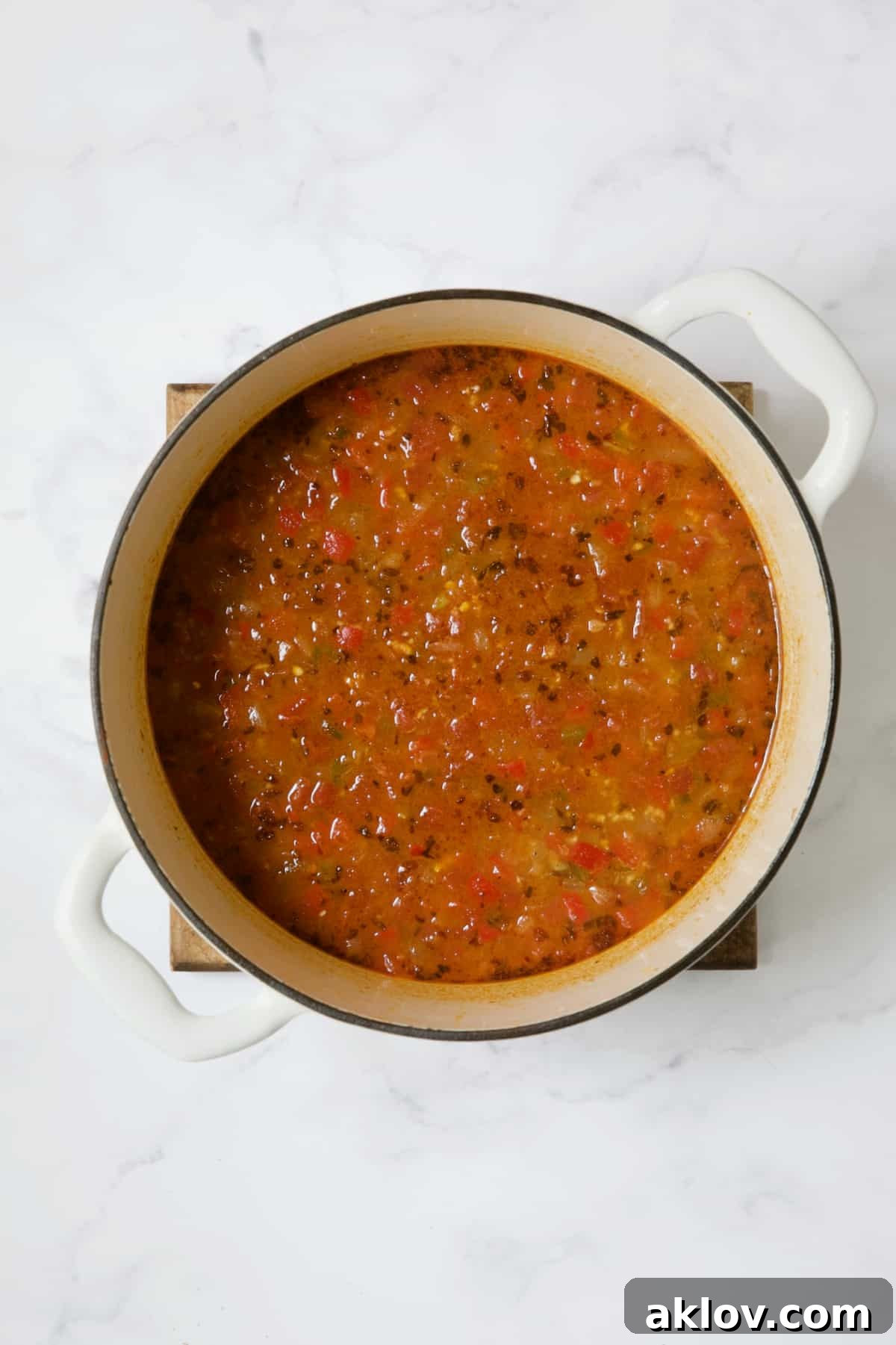 A vibrant red soup base simmering in a white Dutch oven, infused with tomatoes, broth, and spices.