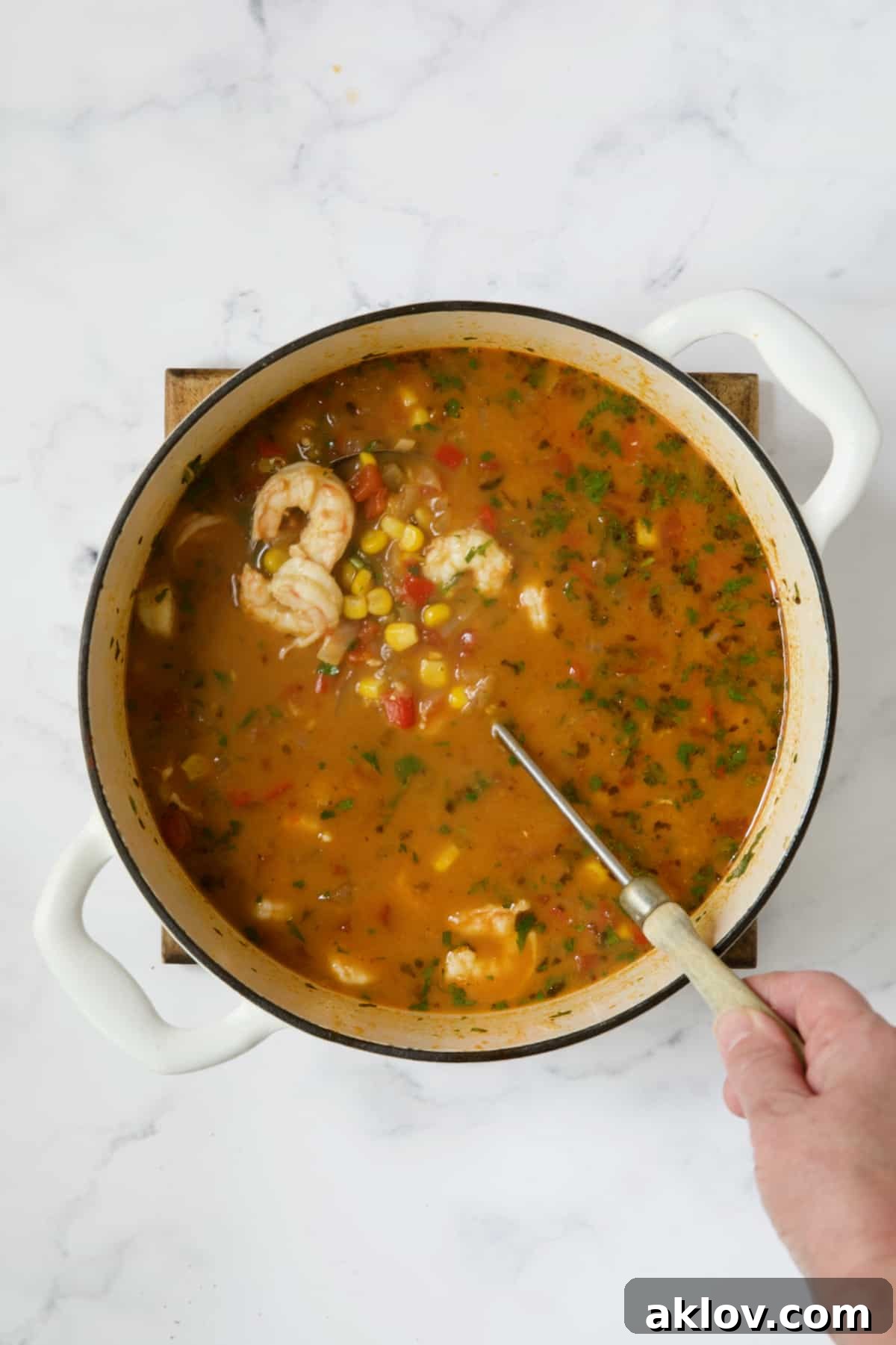 Shrimp and corn being gently stirred into the simmering soup in a white Dutch oven, almost ready to serve.