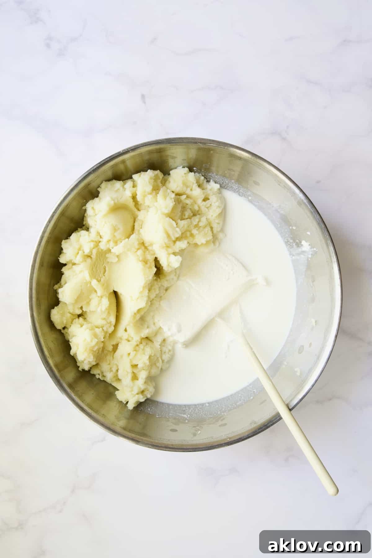 Riced potatoes pushed to one side of a bowl, with cream cheese, sour cream, and half-and-half placed on the other side, ready for blending.