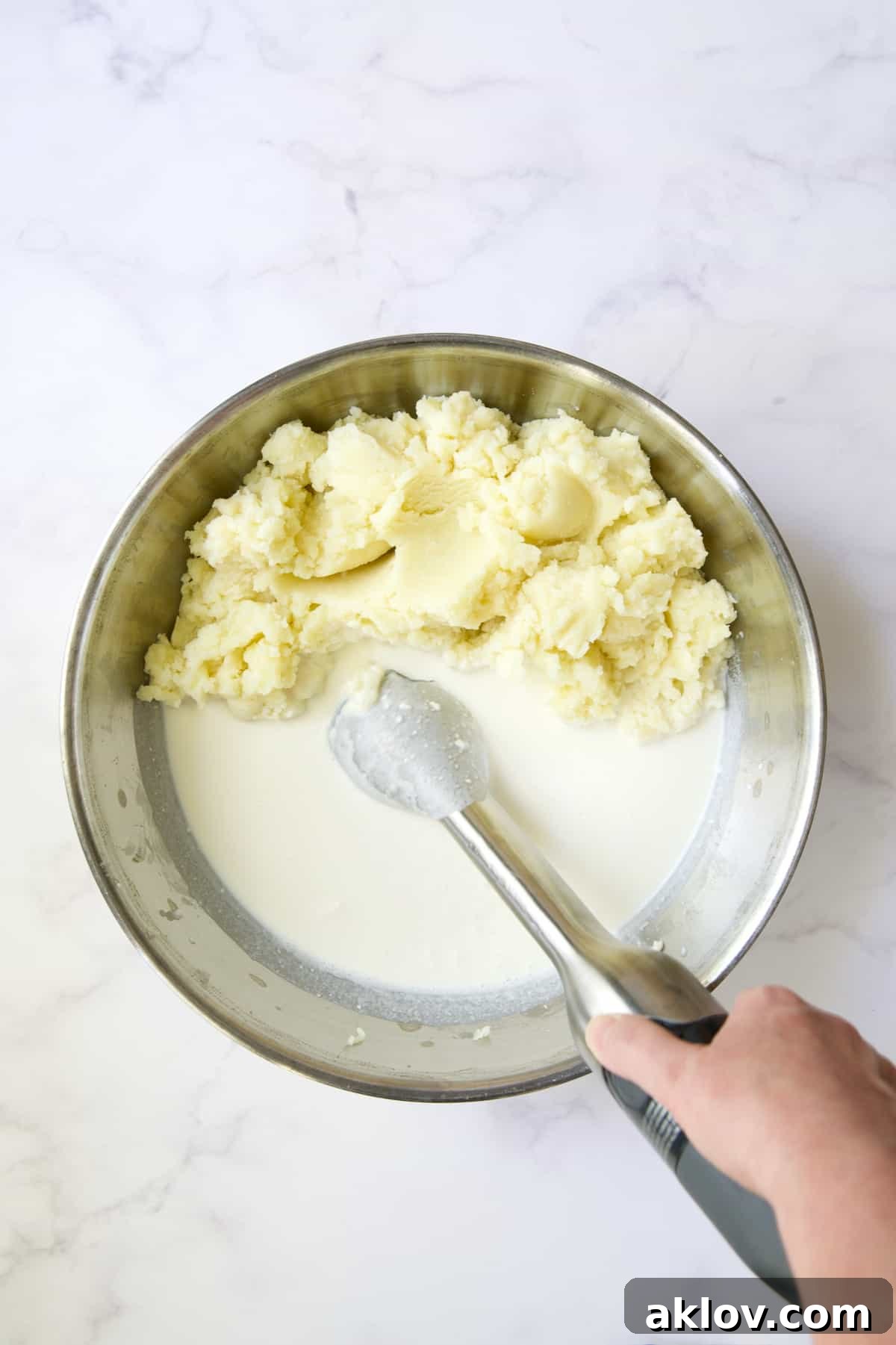 An immersion blender smoothly combining cream cheese, sour cream, and half-and-half in a bowl, creating a perfectly homogenous dairy mixture.