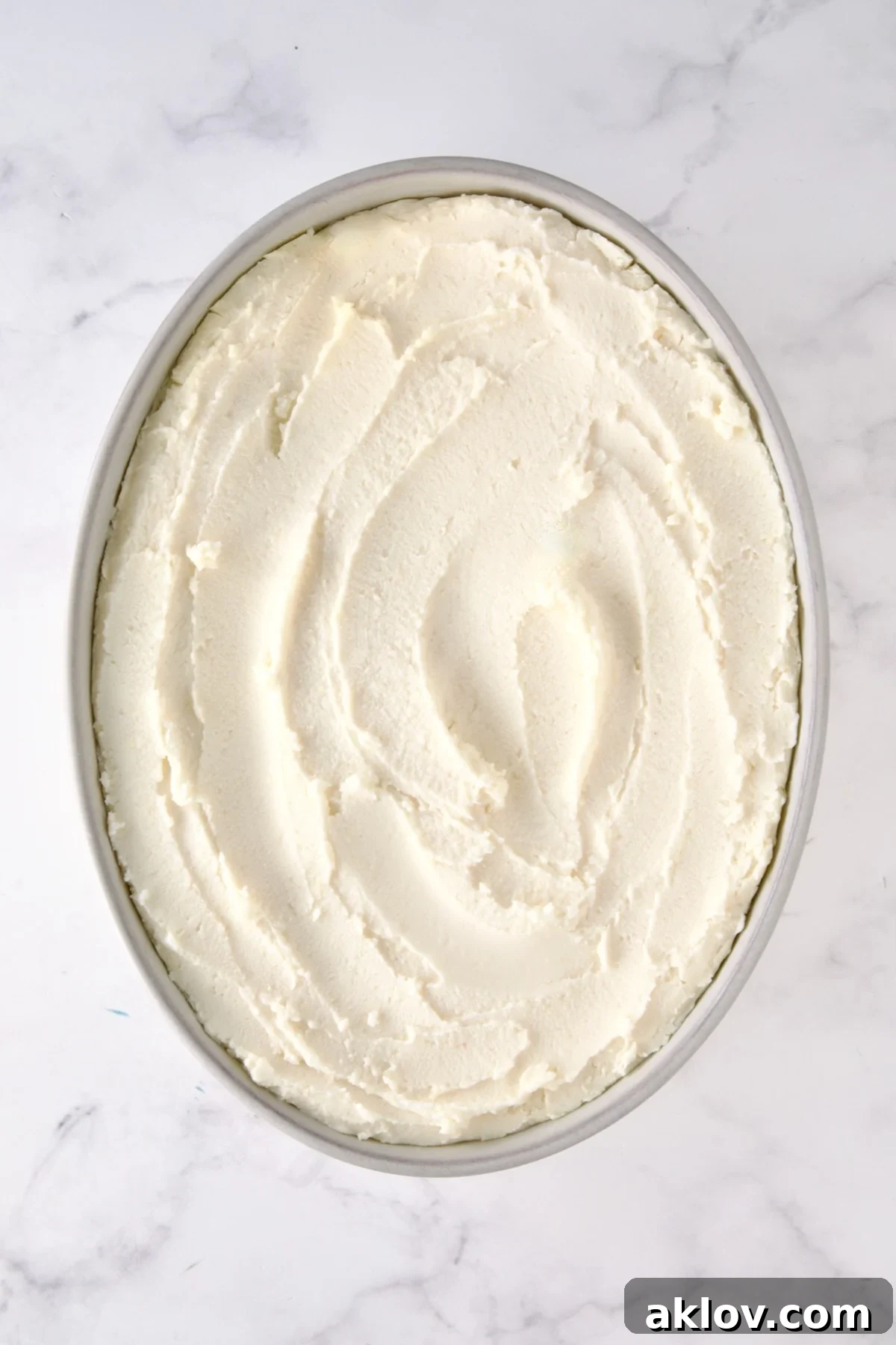 A pristine oval baking dish filled with unbaked mashed potatoes, smoothed and ready for their golden transformation in the oven.