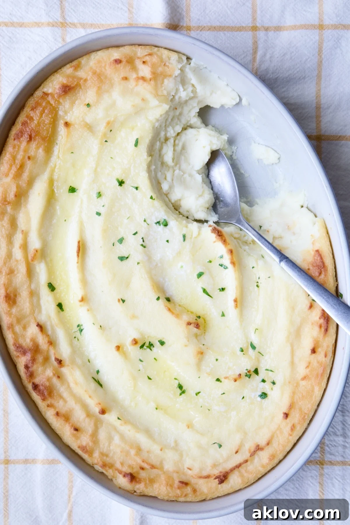 A serving spoon gracefully lifts a fluffy portion of Twice-Baked Mashed Potatoes from an elegant white oval baking dish, highlighting their creamy texture.