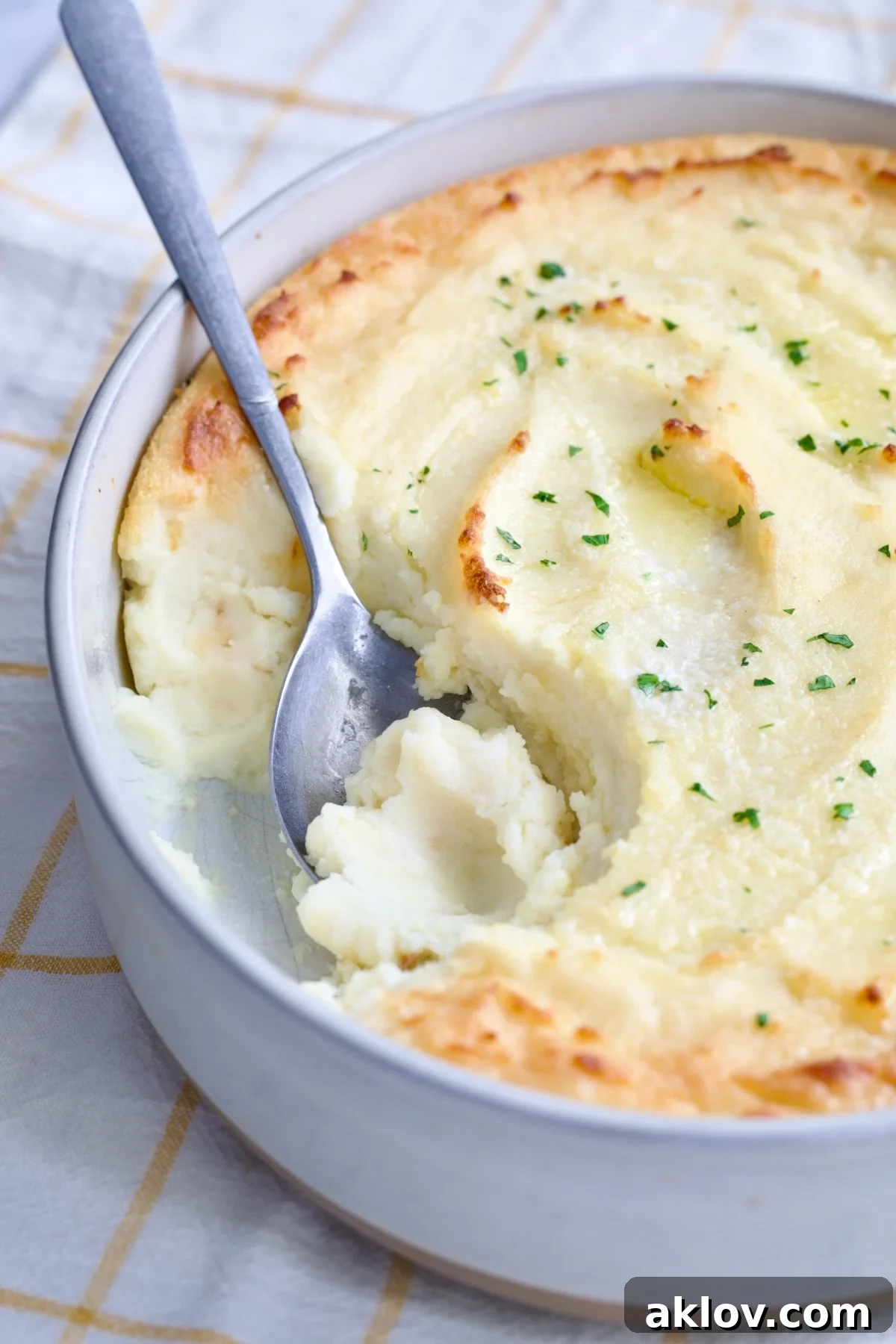 A serving of Twice-Baked Mashed Potatoes being scooped from a white oval baking dish, showing its appealing texture and golden edges.