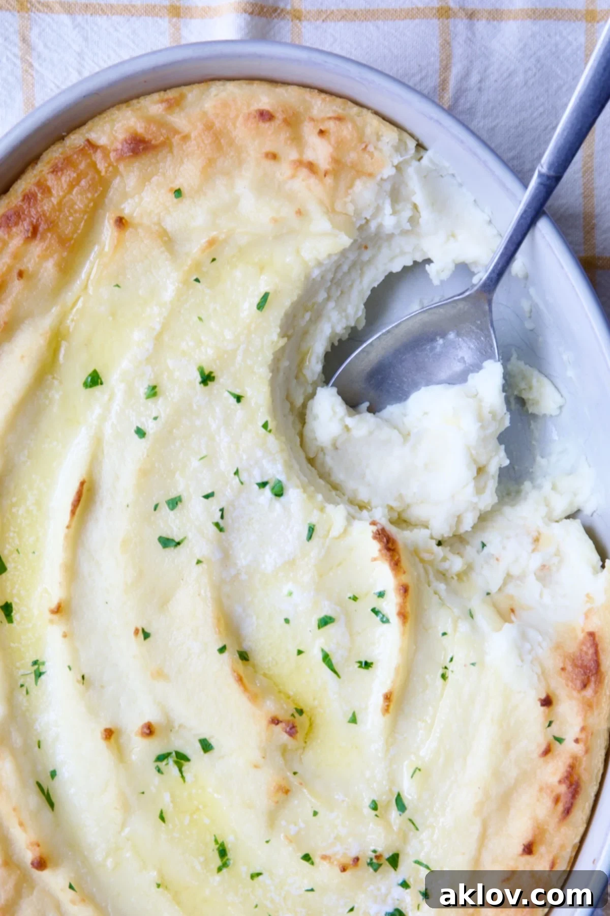 A close-up shot of Twice-Baked Mashed Potatoes in a white oval baking dish, with a serving spoon scooping out a generous portion, emphasizing its inviting texture.