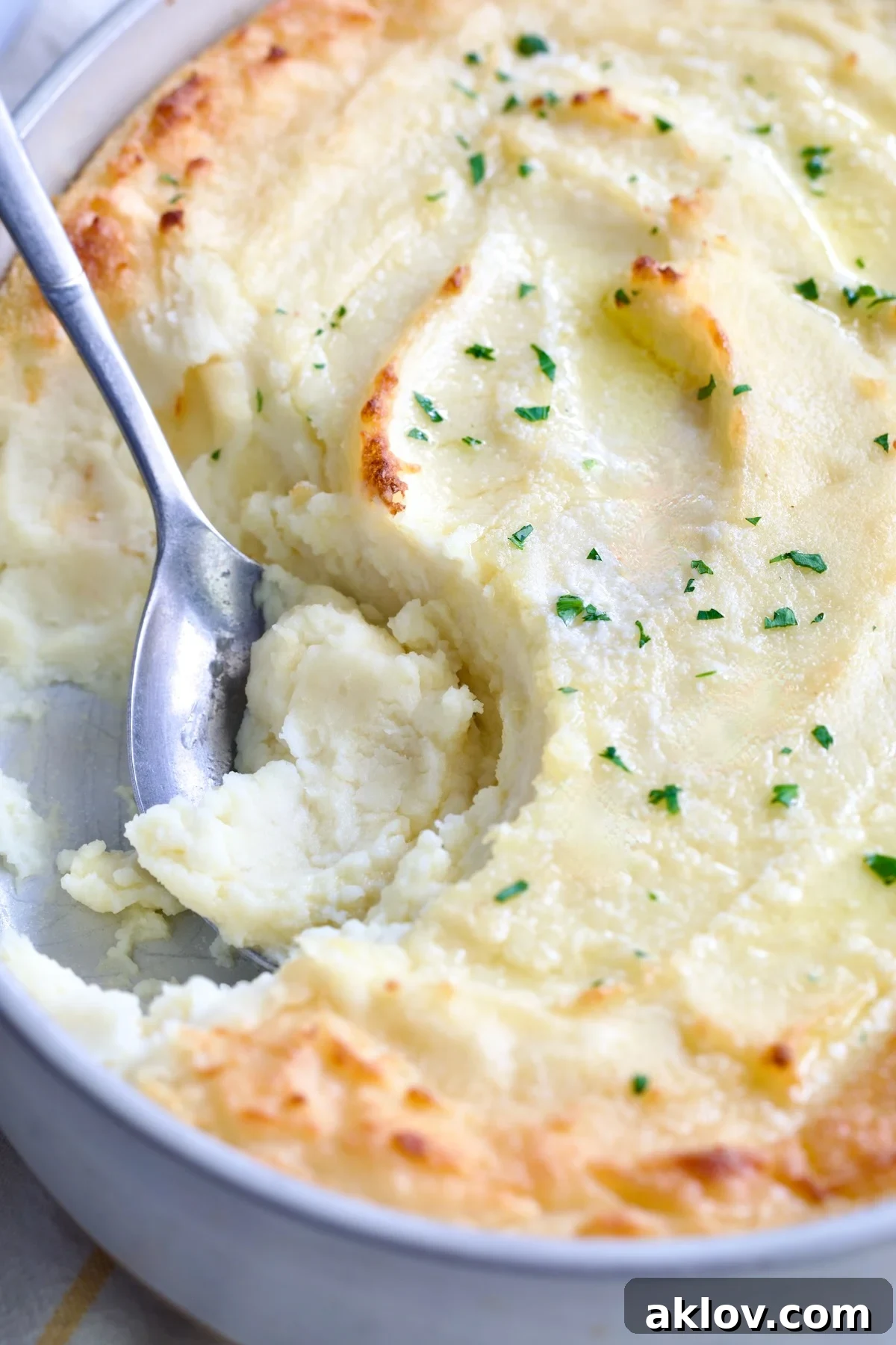 Close-up of fluffy Twice-Baked Mashed Potatoes in a white oval baking dish, with a serving spoon scooping a portion.