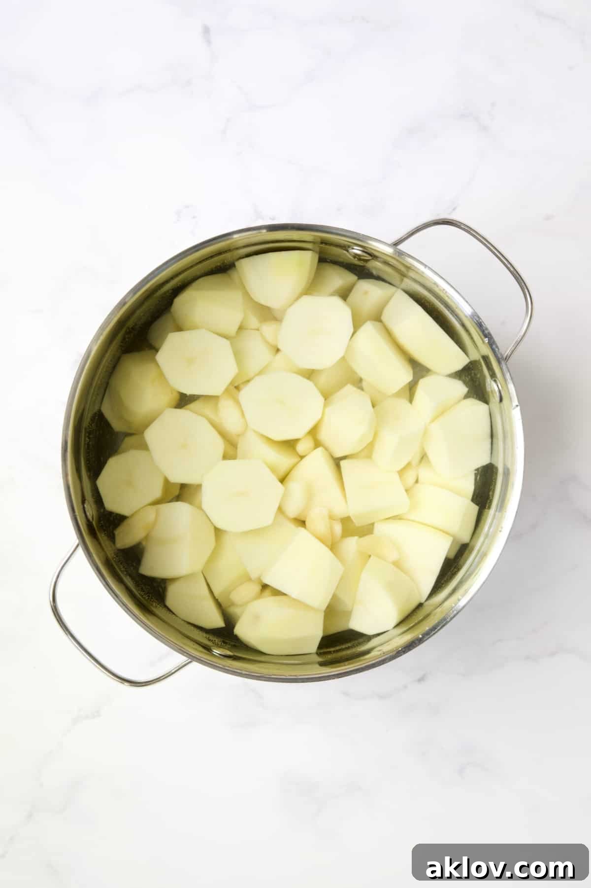 Roughly chopped Russet potatoes and garlic cloves submerged in cold, salted water in a large pot, ready for boiling.