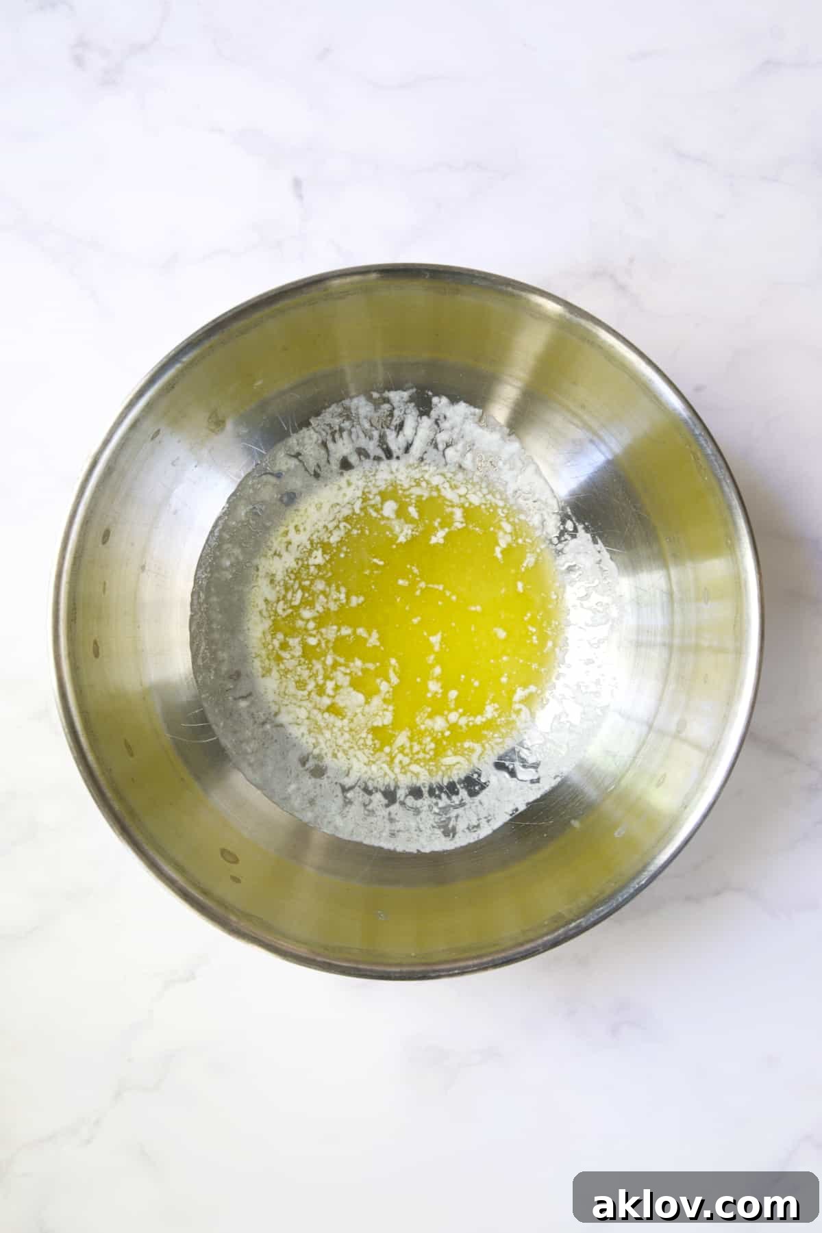 Perfectly melted unsalted butter collected in a stainless steel bowl, ready for use.
