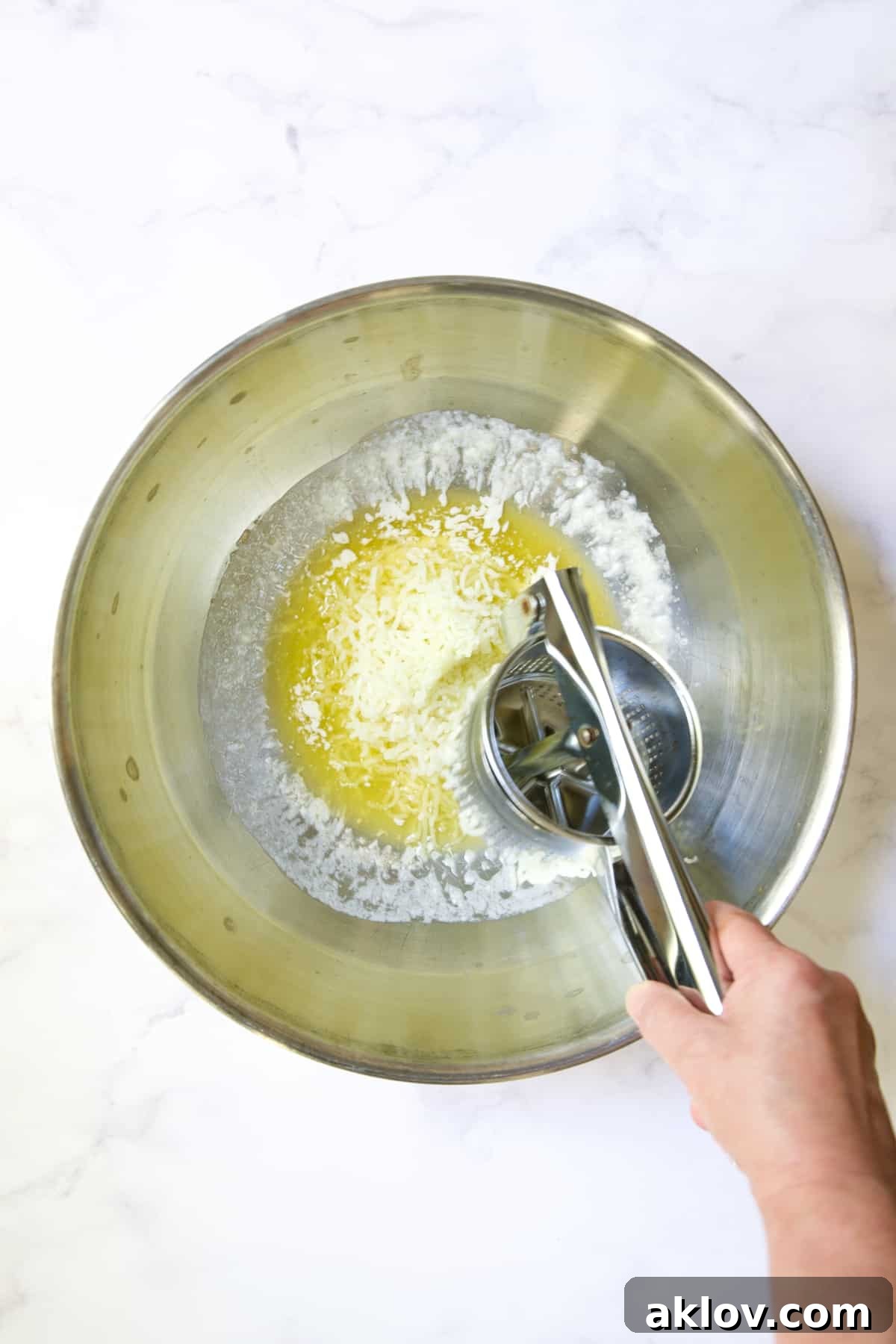 Riced potatoes gracefully falling into melted butter within a stainless steel bowl, beginning the process of flavor infusion.