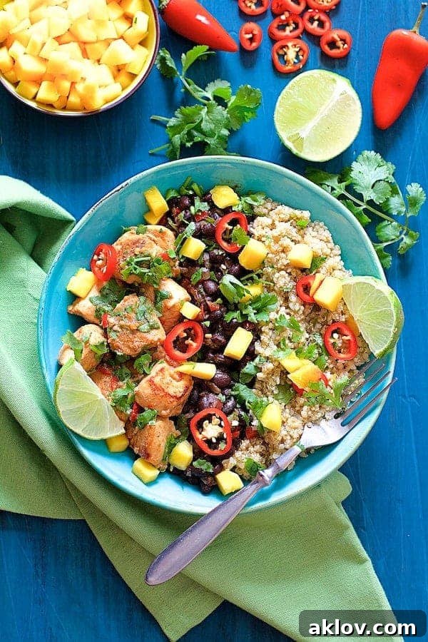 Vibrant Cuban Chicken and Black Bean Quinoa Bowls in a bright blue bowl, garnished with fresh mango, lime wedges, cilantro, and red chiles, set against a blue background on a green napkin.