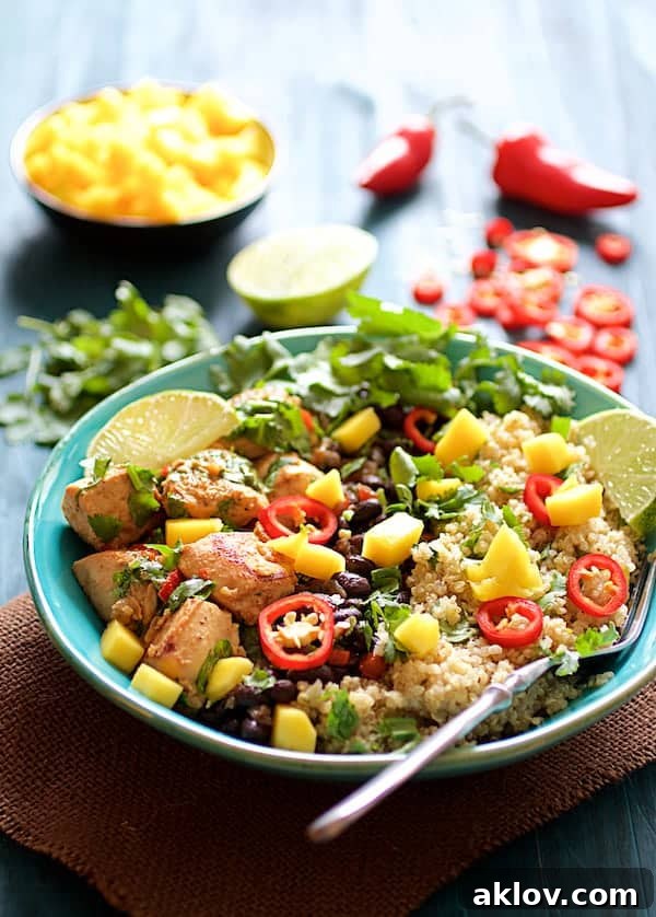 Close-up photo of Cuban Chicken and Black Bean Quinoa Bowls, garnished with fresh mango, lime wedges, cilantro, and a vibrant Fresno chile, offering a tropical culinary aesthetic.