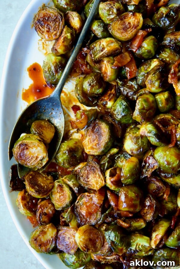 Maple Bacon Gochujang Brussels Sprouts on a white platter with a serving fork, glistening with glaze.