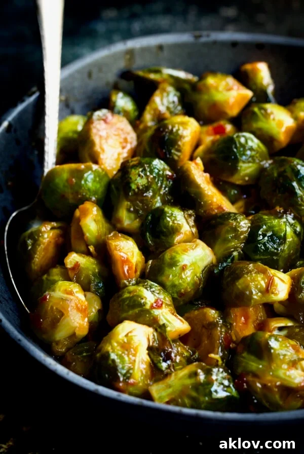 Sriracha Sweet Chili Roasted Brussels Sprouts in a gray speckled bowl with a serving spoon, highlighting their crispy texture.