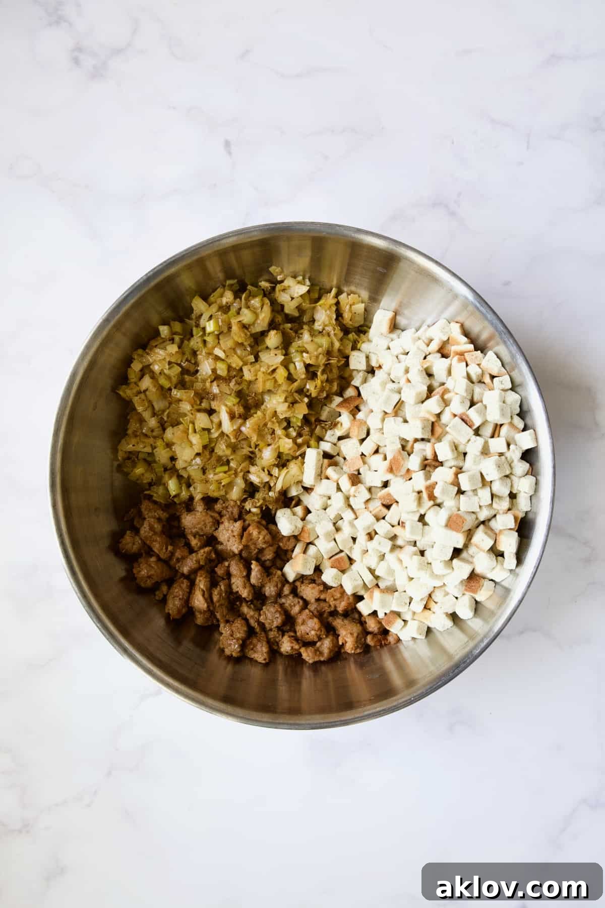 Individual cooked ingredients for Sausage Stuffing with Fennel and Leeks arranged in a stainless steel bowl before being thoroughly mixed.