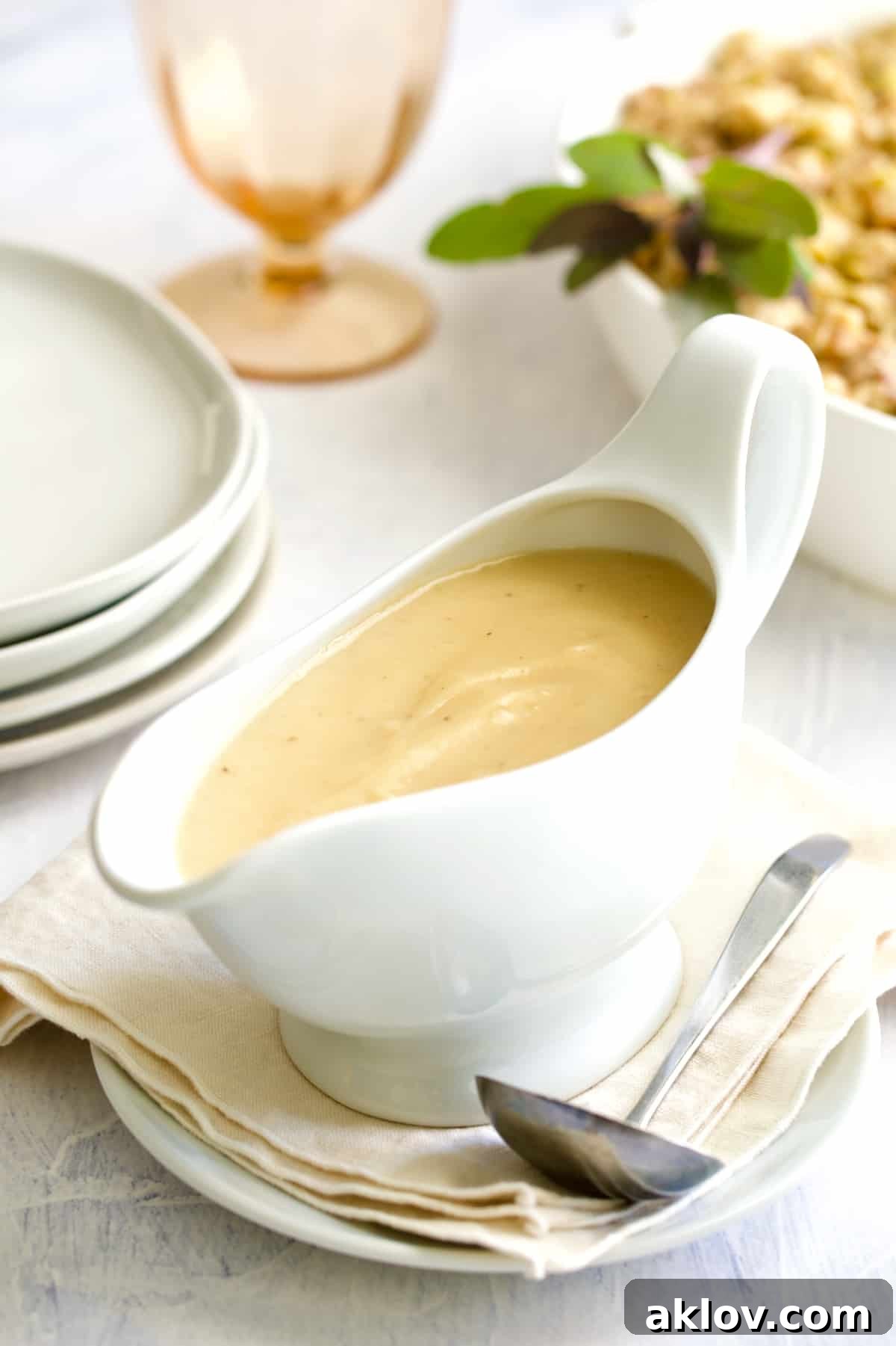 Gravy in white gravy boat on beige napkin with ladle, showcasing its rich texture and color.