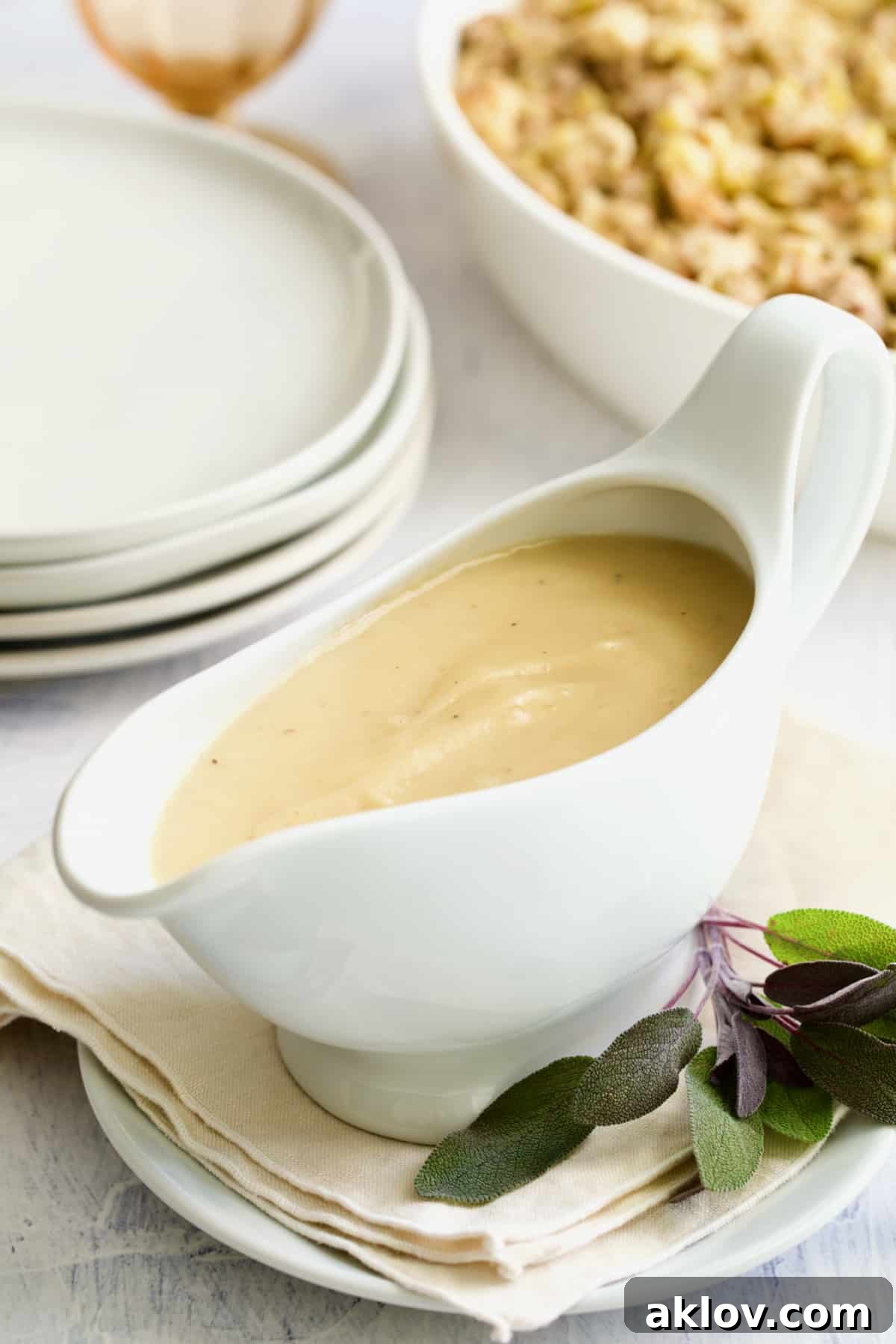 Elegant white gravy boat filled with rich gravy, garnished with a sprig of fresh sage, resting on a beige napkin.
