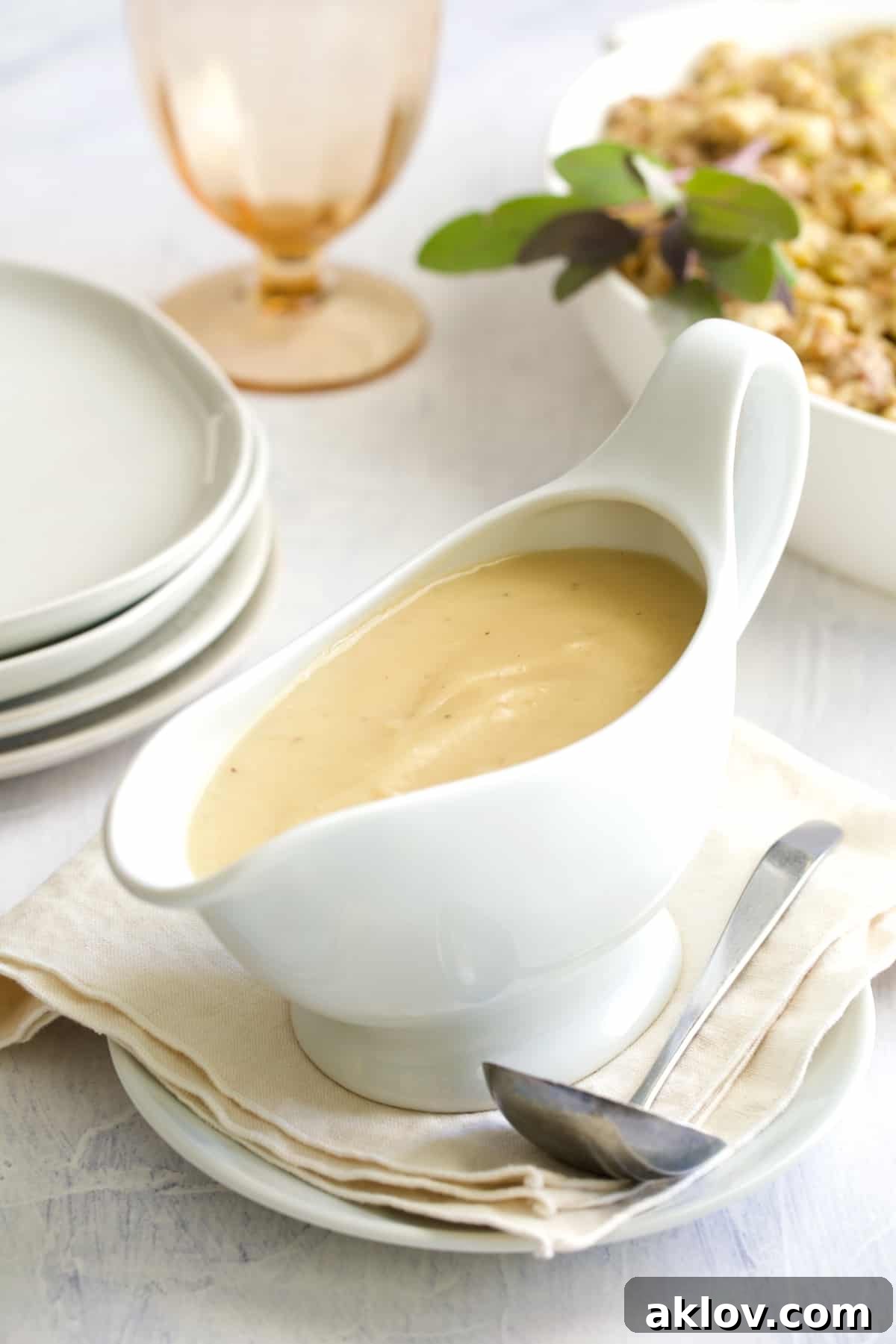A festive holiday table setting with a white gravy boat full of gravy, plates, wine glass, and stuffing in the background, ready for a meal.
