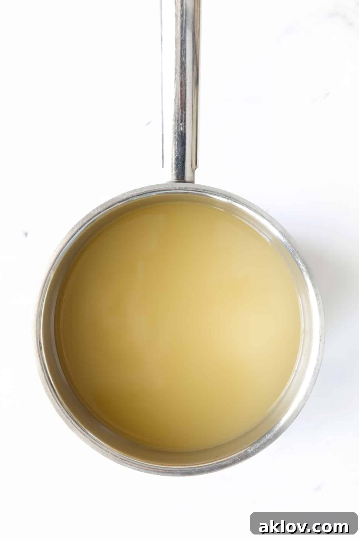 Clear chicken broth fills a gleaming stainless steel saucepan, ready for the reduction process.