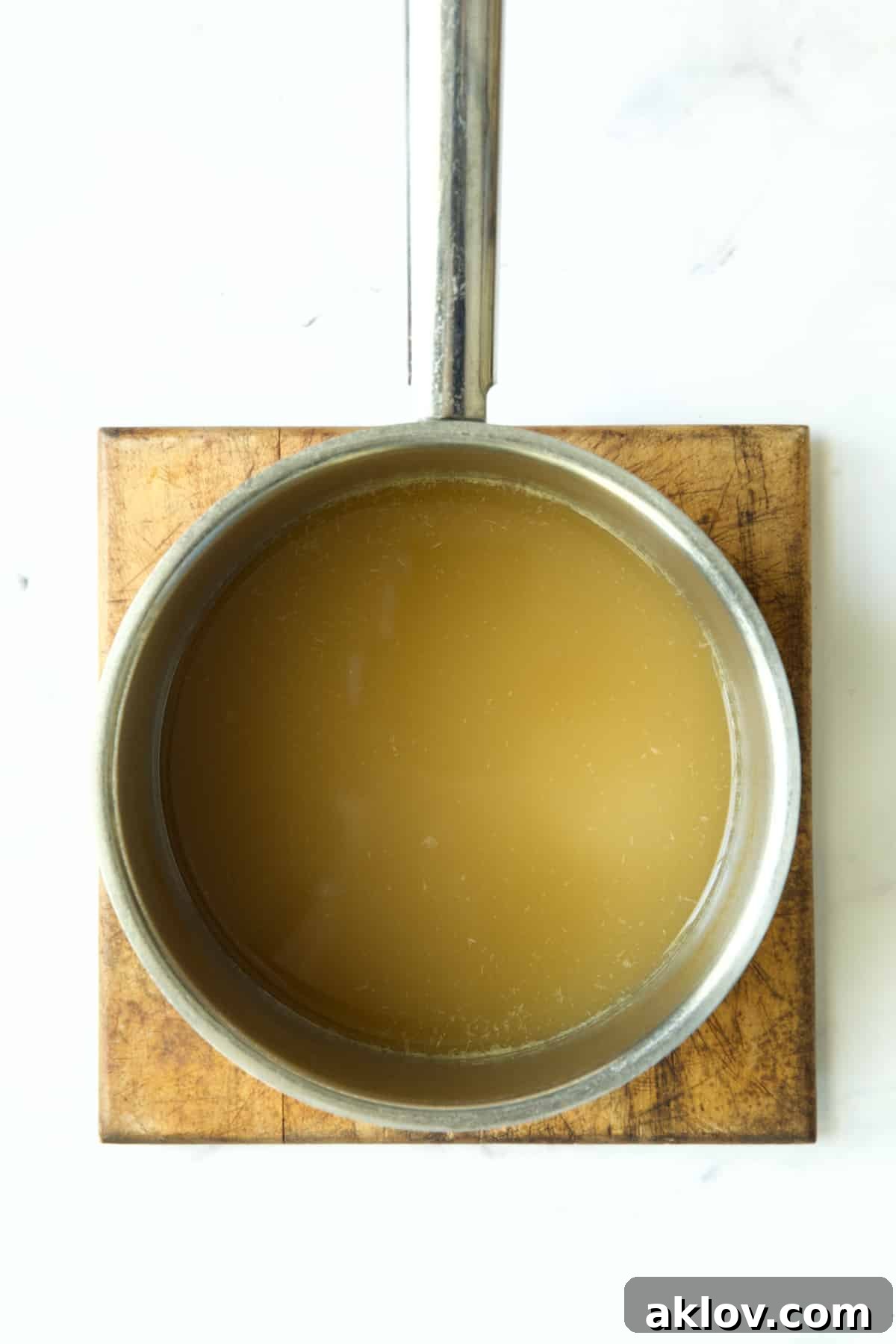The chicken broth in a stainless steel saucepan is noticeably reduced, having simmered down to intensify its flavor.