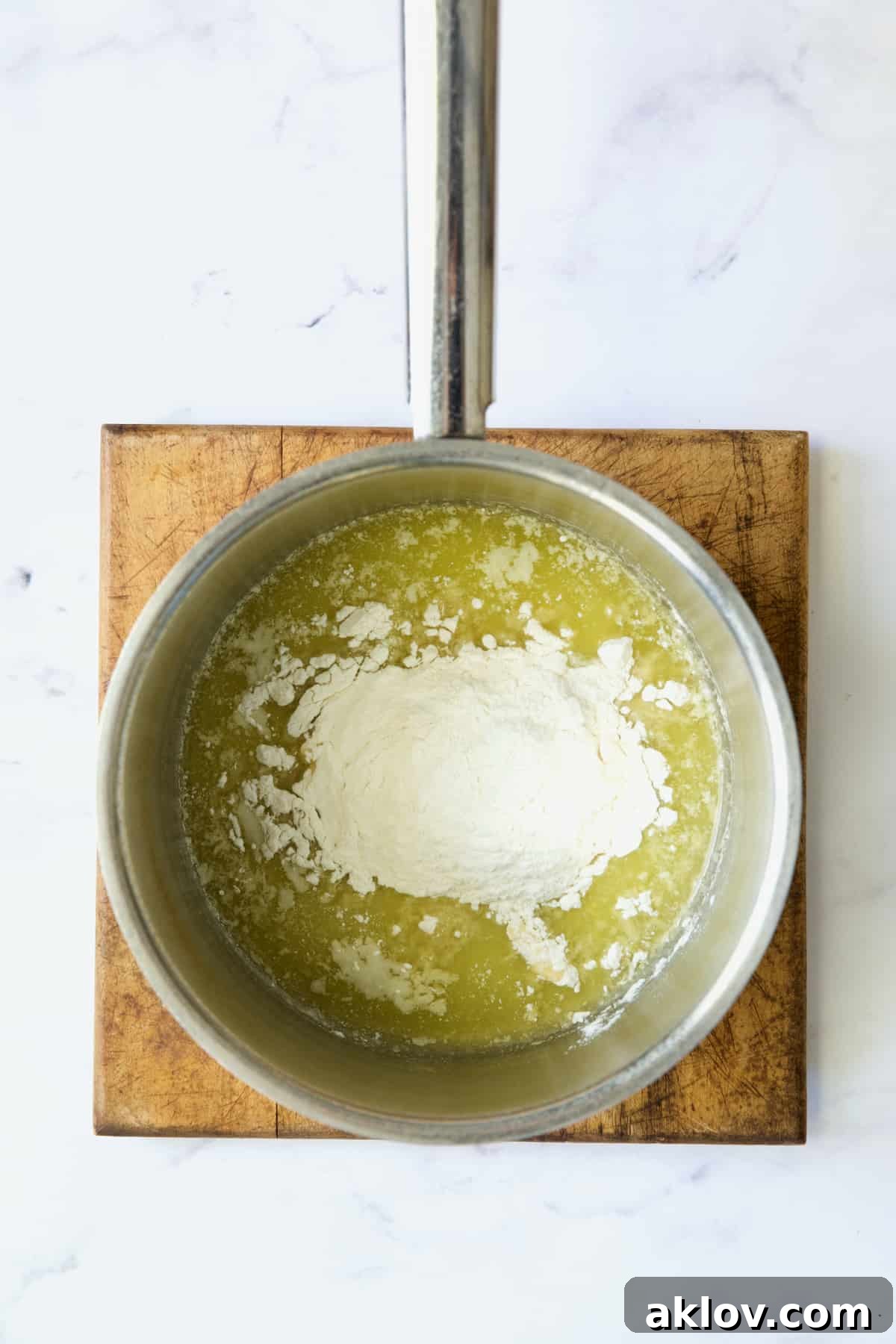 Flour has just been added to the melted butter in a stainless steel saucepan, forming the beginnings of a roux.