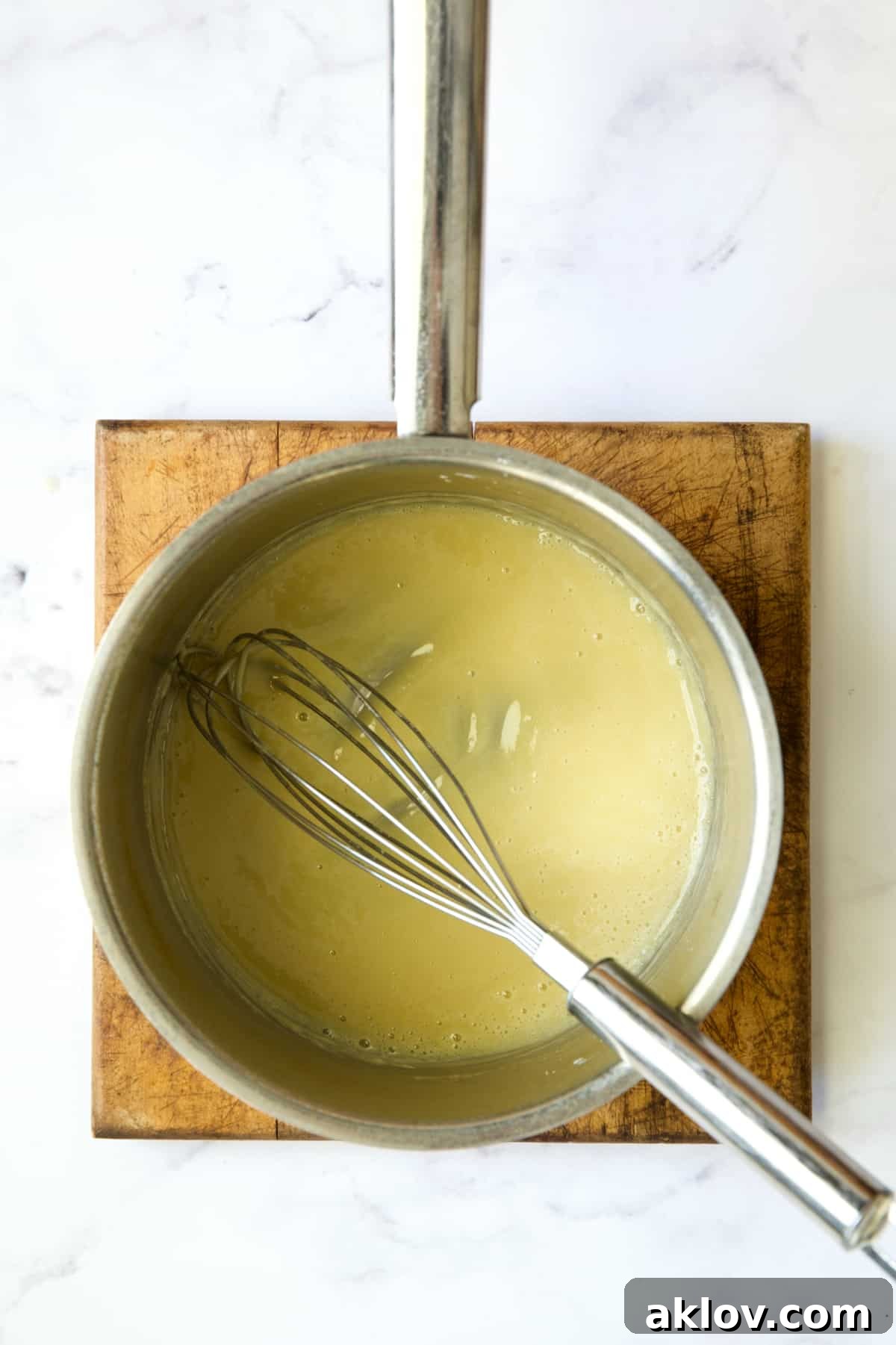 A whisk vigorously mixes butter and flour in a stainless steel saucepan, creating a smooth roux.