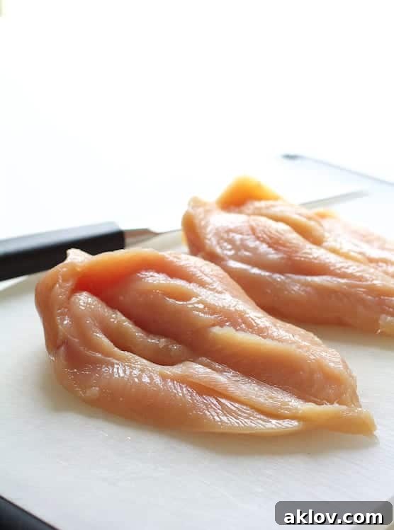 Photo illustrating the technique of butterflying chicken breasts on a cutting board, preparing them for stuffing.