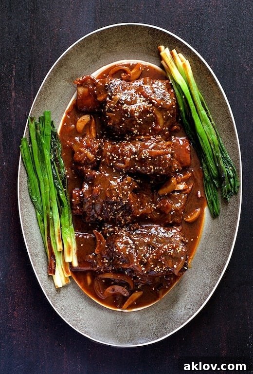 Photo of Korean Braised Beef Short Ribs on gray-rimmed platter garnished with scallions and sesame seeds.