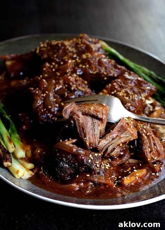 Photo of Korean Braised Beef Short Ribs on gray-rimmed platter being shredded with fork.