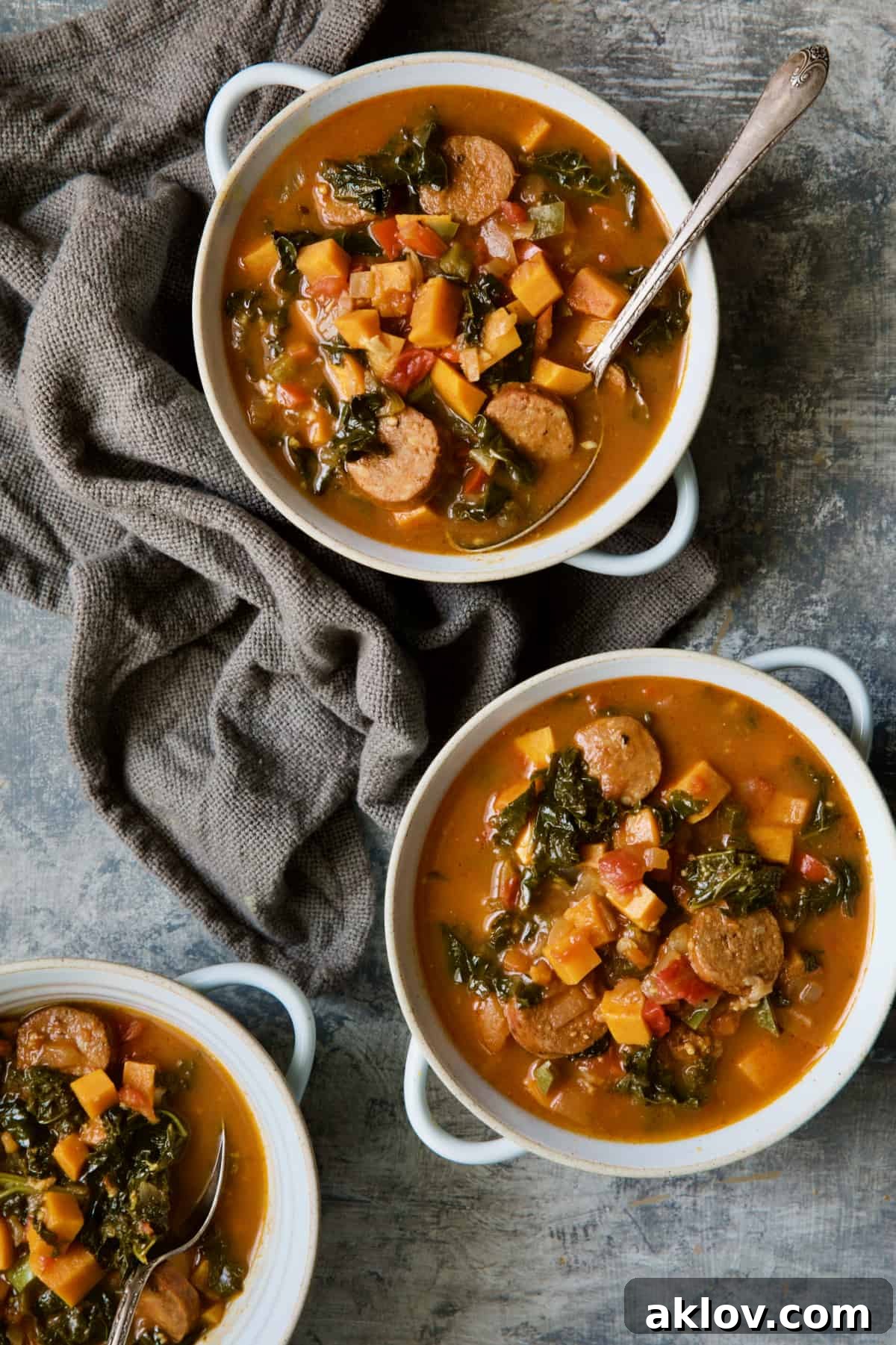 Chorizo Sweet Potato Stew with Kale in white bowls with soup spoon on gray background.