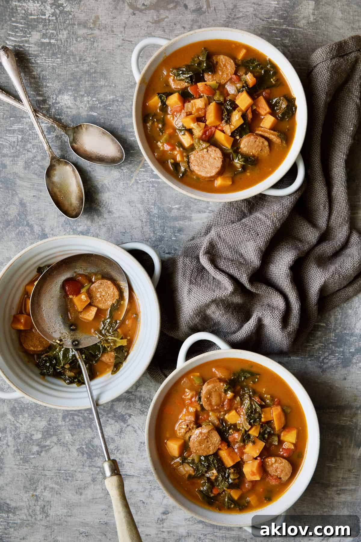 Three bowls of Chorizo Sweet Potato Stew with Kale on gray background with soup spoons.