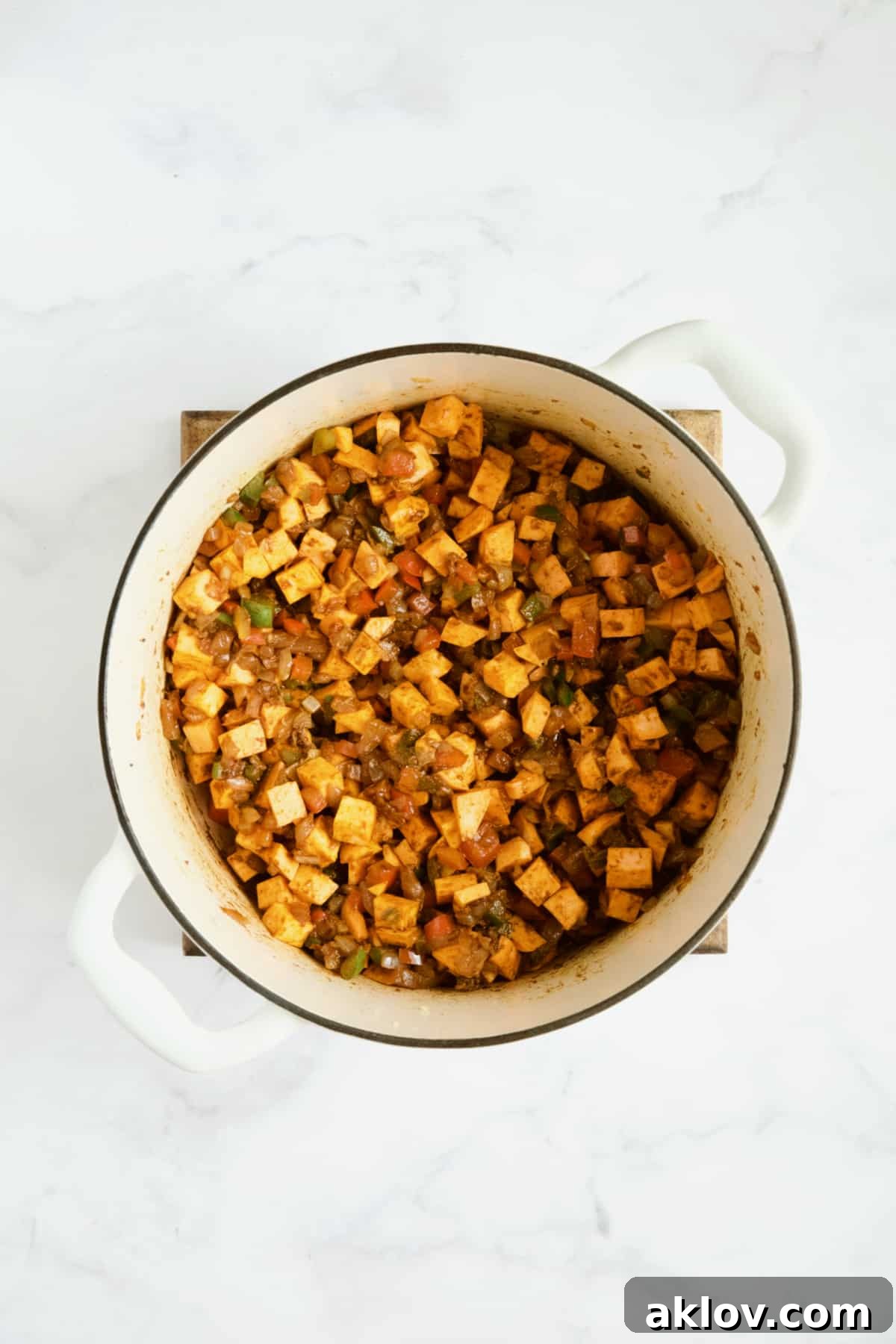 Sweet potatoes added to vegetables being cooked in white Dutch oven.