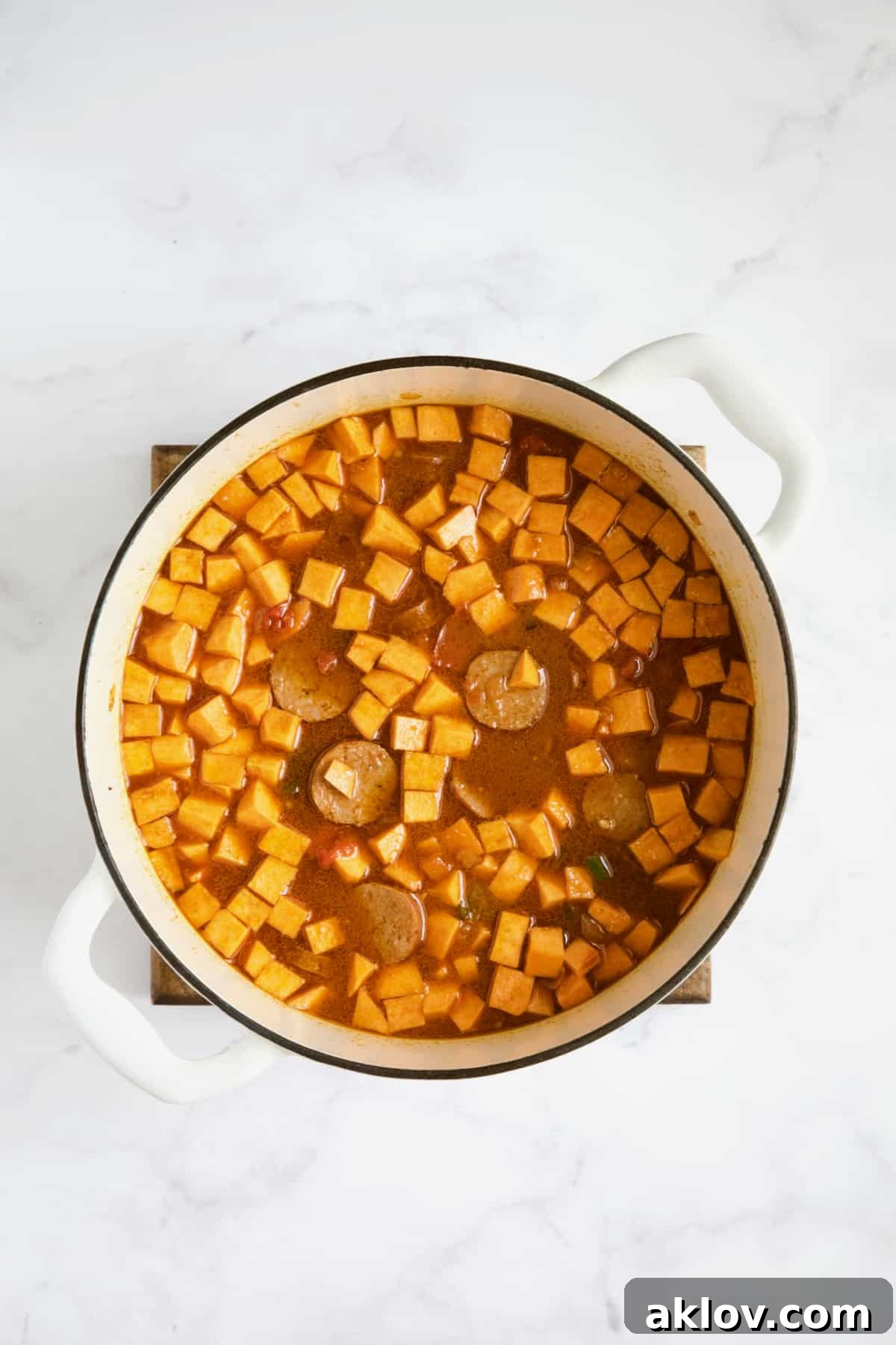 Sweet potatoes and chorizo added to stew in white Dutch oven.