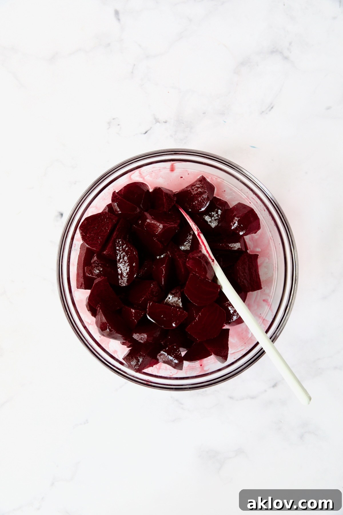 Roasted beets being gently stirred and coated with the red wine glaze in a clear glass bowl.