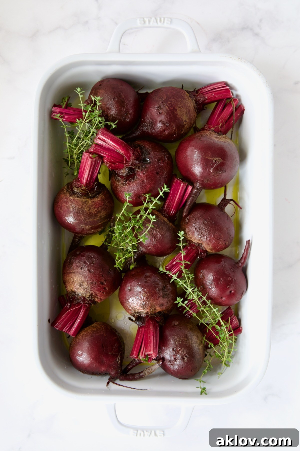 Raw beets and thyme sprigs arranged in a white rectangular roasting dish, ready for the oven.
