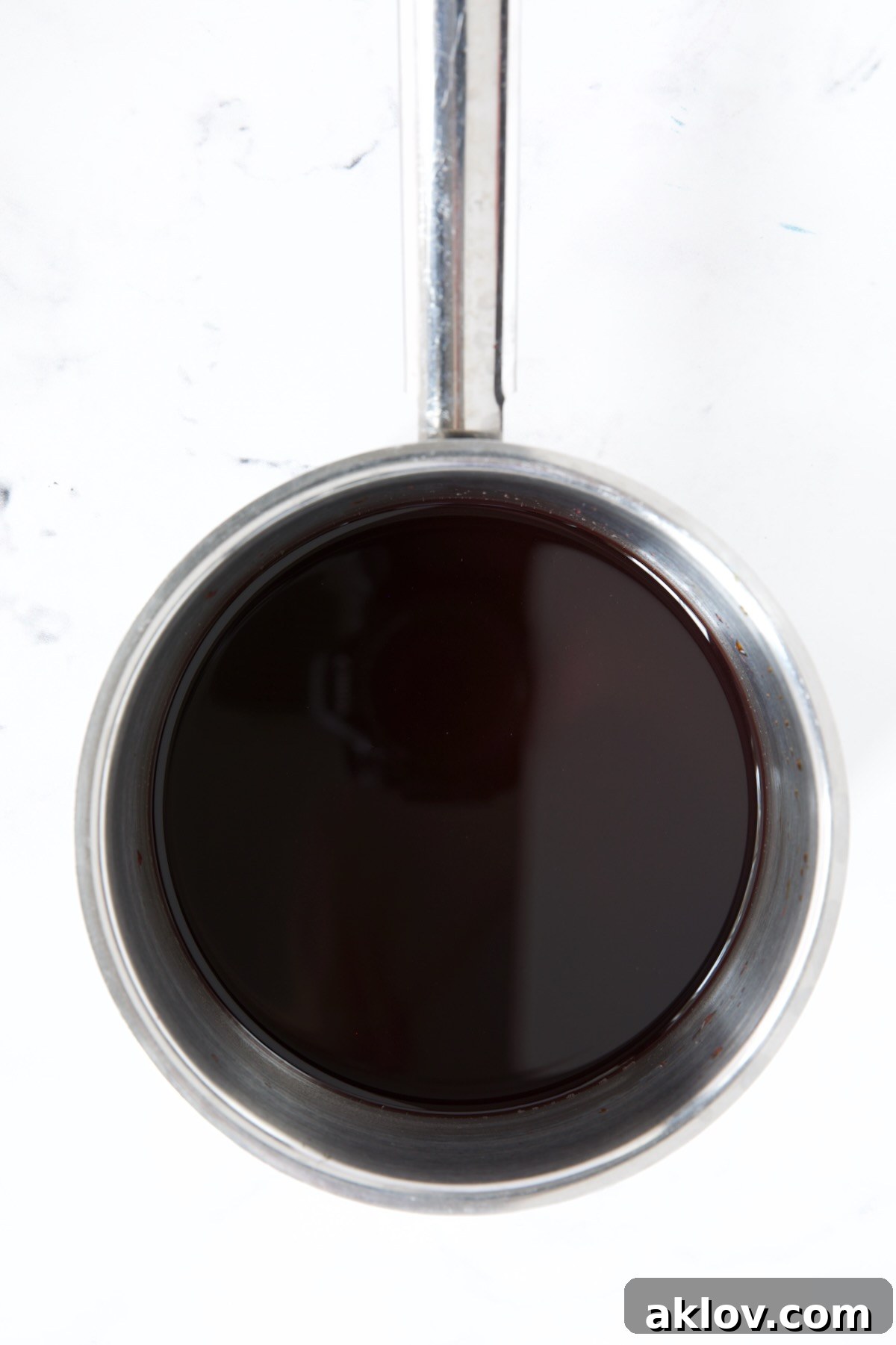 Rich red wine glaze simmering in a stainless steel saucepan, thickening to a syrupy consistency.