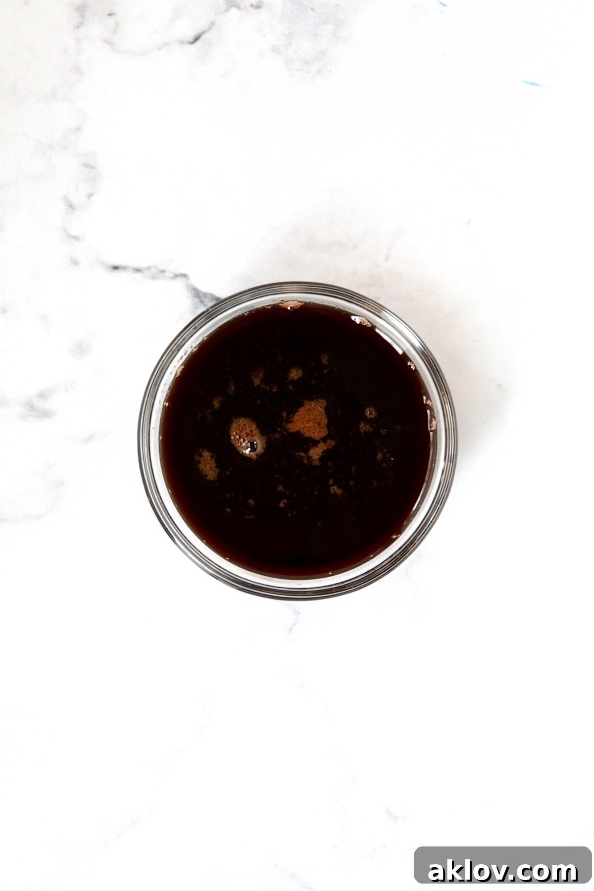The finished red wine glaze, thick and glossy, ready to be poured, presented in a clear glass bowl.