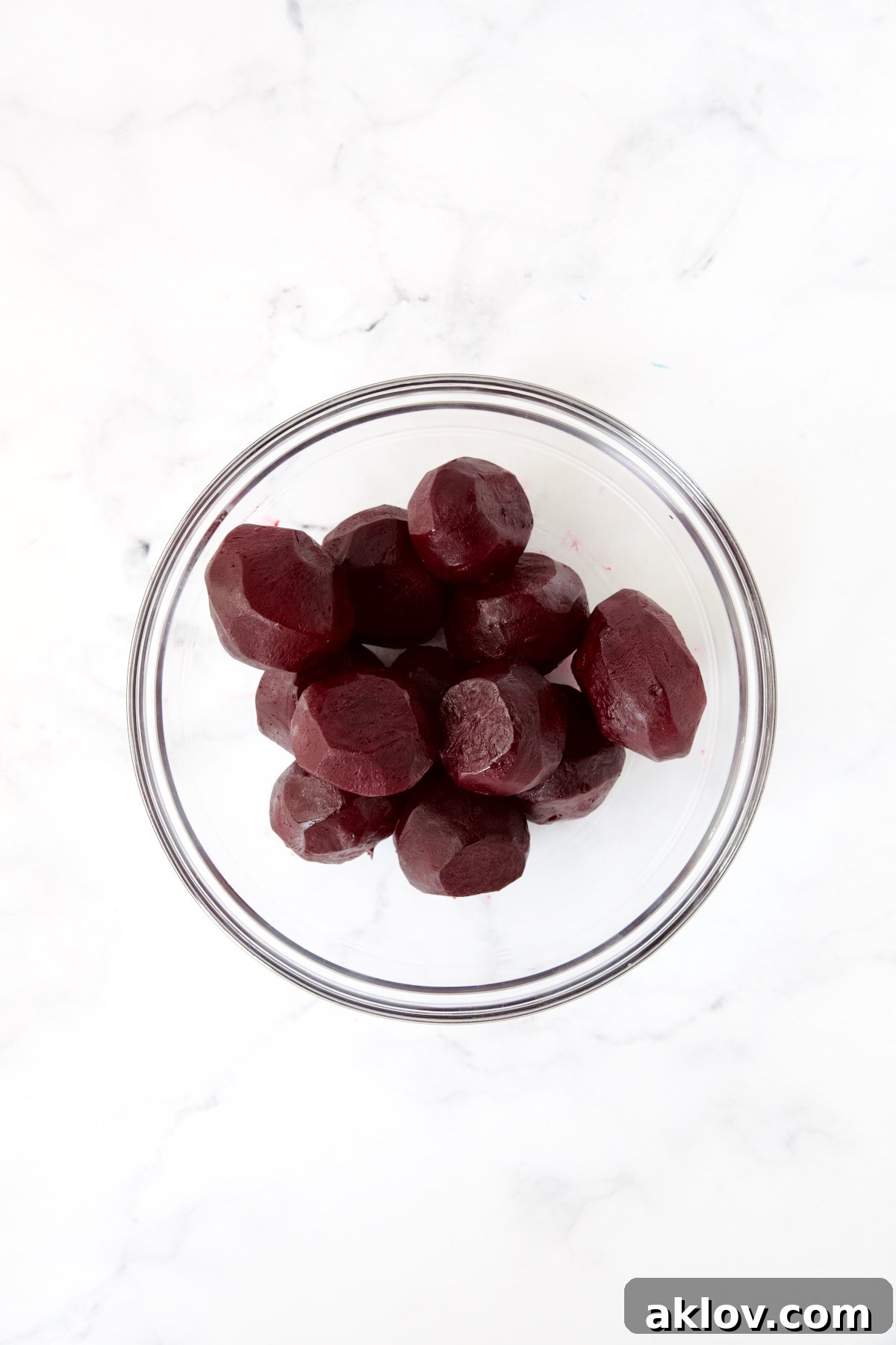 Whole peeled roasted beets, smooth and vibrant, presented in a clear glass bowl.