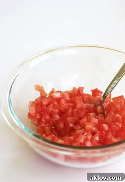 Pan-Seared Scallops with Vibrant Balsamic Tomato Salsa 14 Photo of diced tomatoes in glass mixing bowl being stirred with spoon.