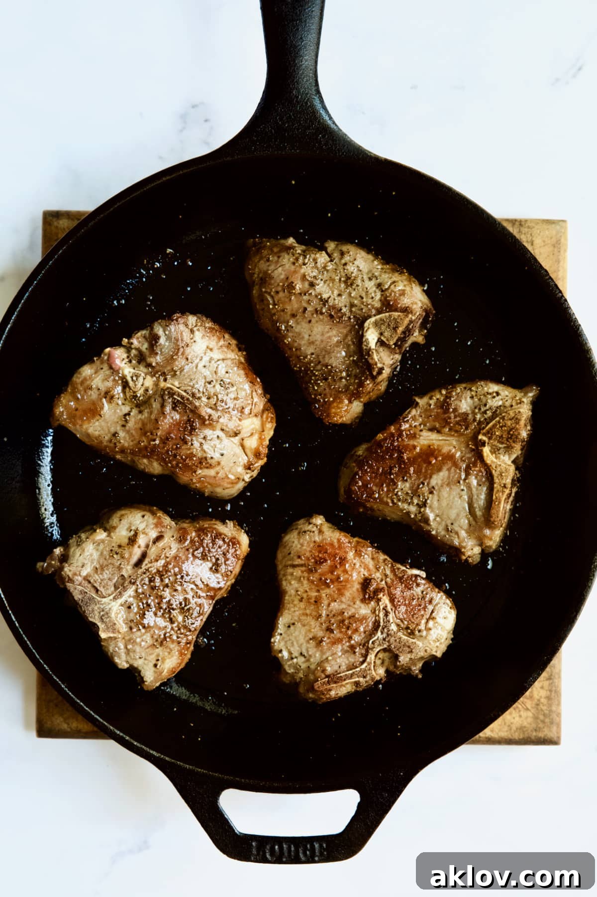 Five beautifully seared lamb chops cooking in a robust cast iron skillet.