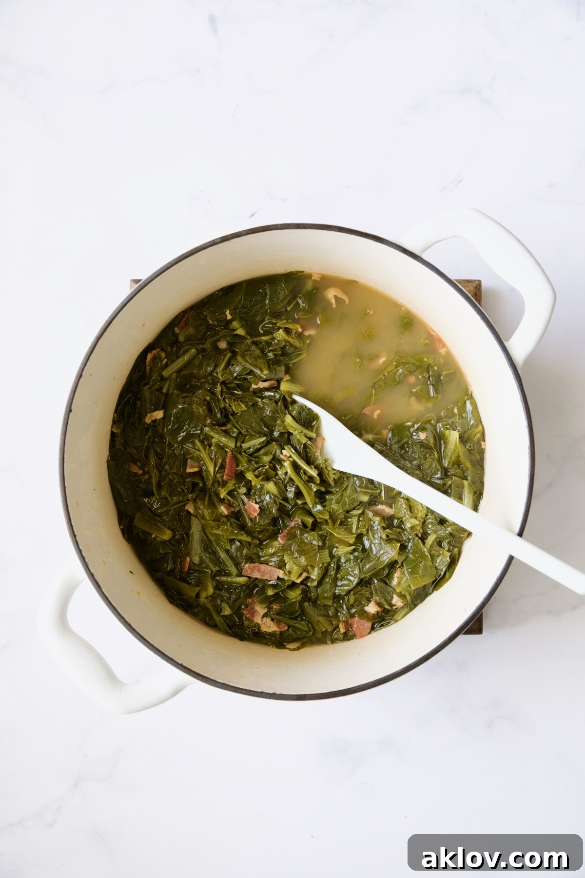 Greens in white Dutch oven being stirred with white spoon.